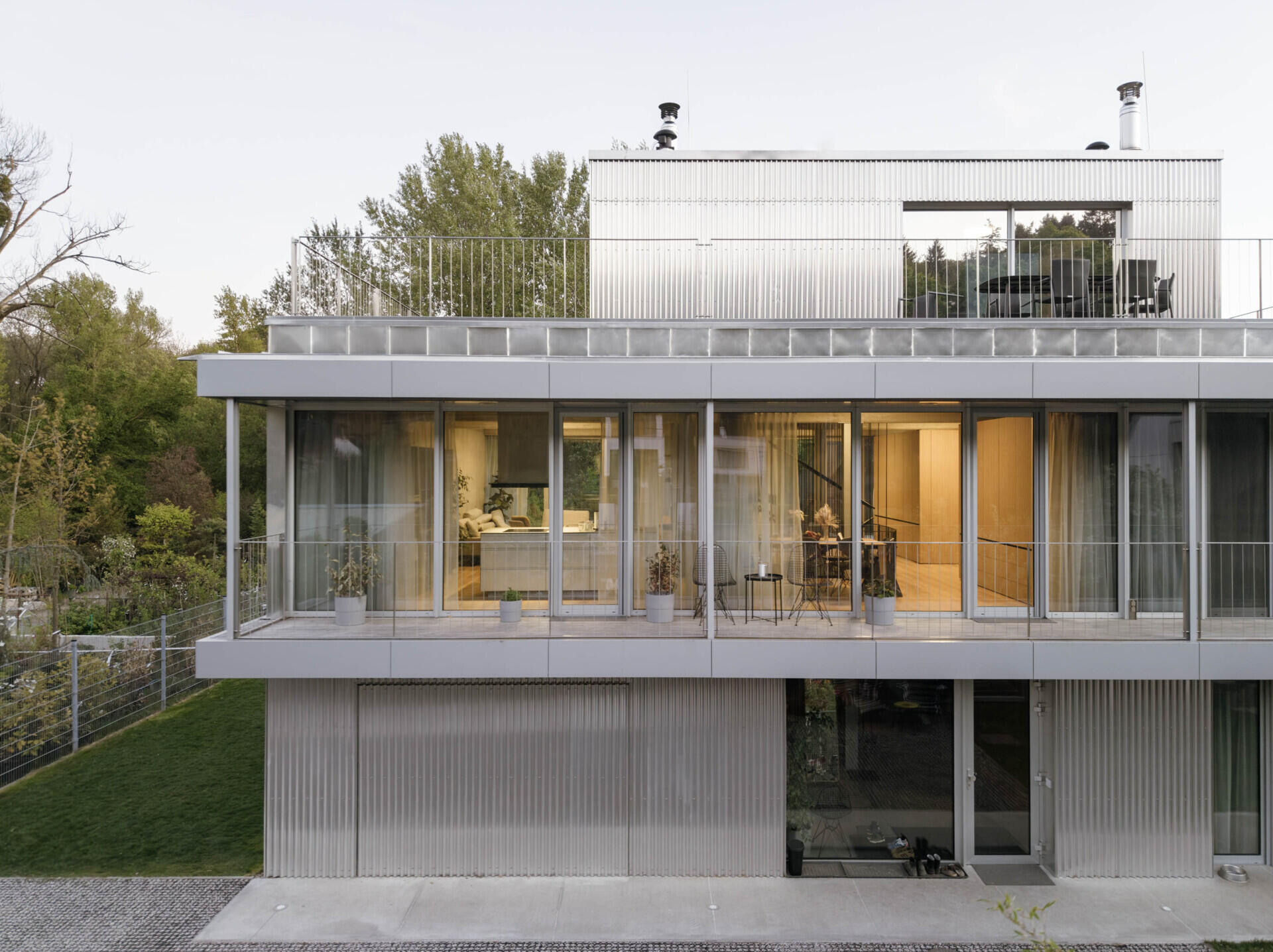 Set between the Carpathian foothills and the Danube River, this modern house features elevated living spaces, flexible interiors, panoramic views, a rooftop terrace, and a reflective raw aluminum facade that changes with the light throughout the day.