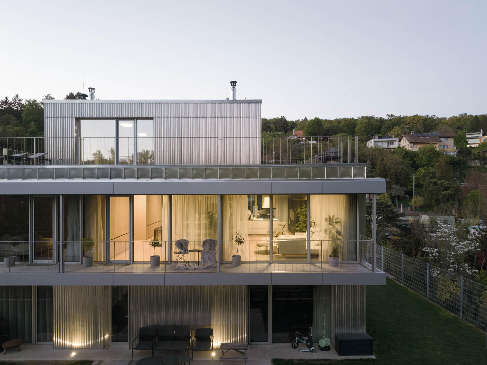Set between the Carpathian foothills and the Danube River, this modern house features elevated living spaces, flexible interiors, panoramic views, a rooftop terrace, and a reflective raw aluminum facade that changes with the light throughout the day.