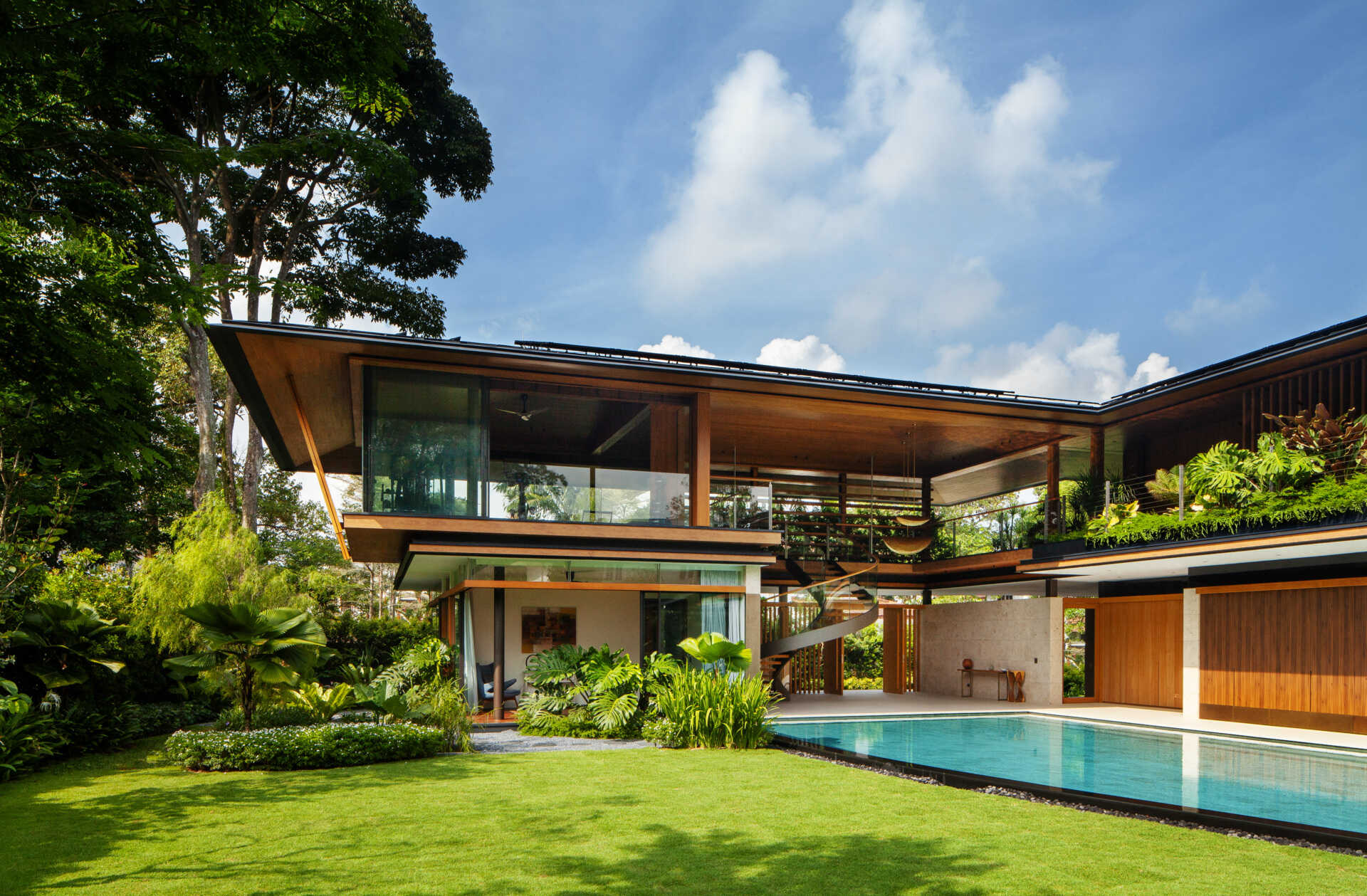 A tropical residence designed around a private courtyard garden. Featuring warm timber interiors, dramatic rooflines, a long swimming pool, lush landscaping, glass walls, and a sculptural spiral staircase, this modern home showcases the beauty of indoor-outdoor living in a tropical climate.