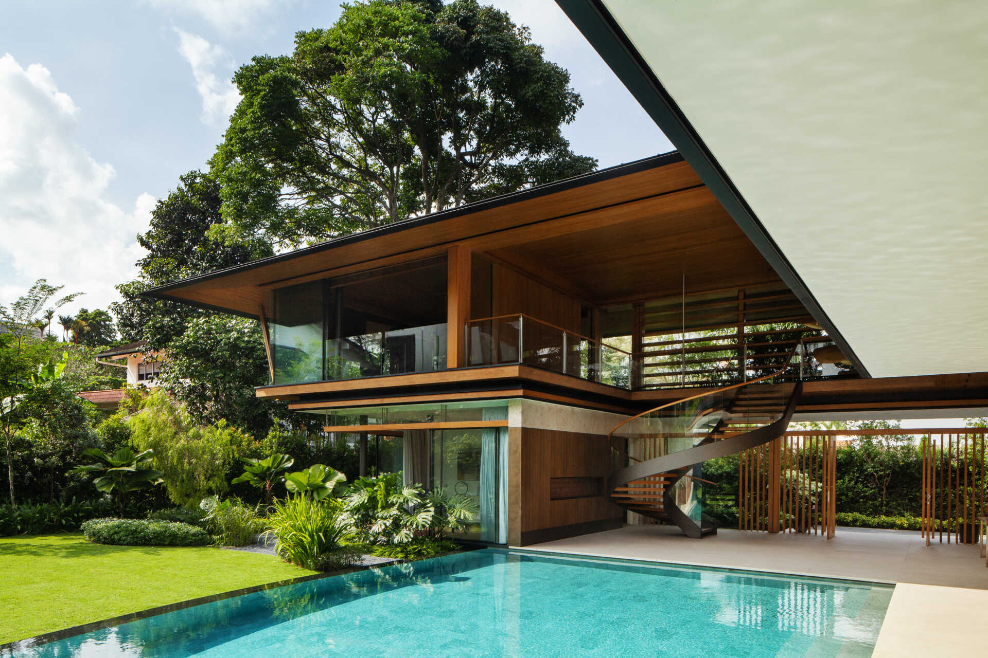 A tropical residence designed around a private courtyard garden. Featuring warm timber interiors, dramatic rooflines, a long swimming pool, lush landscaping, glass walls, and a sculptural spiral staircase, this modern home showcases the beauty of indoor-outdoor living in a tropical climate.