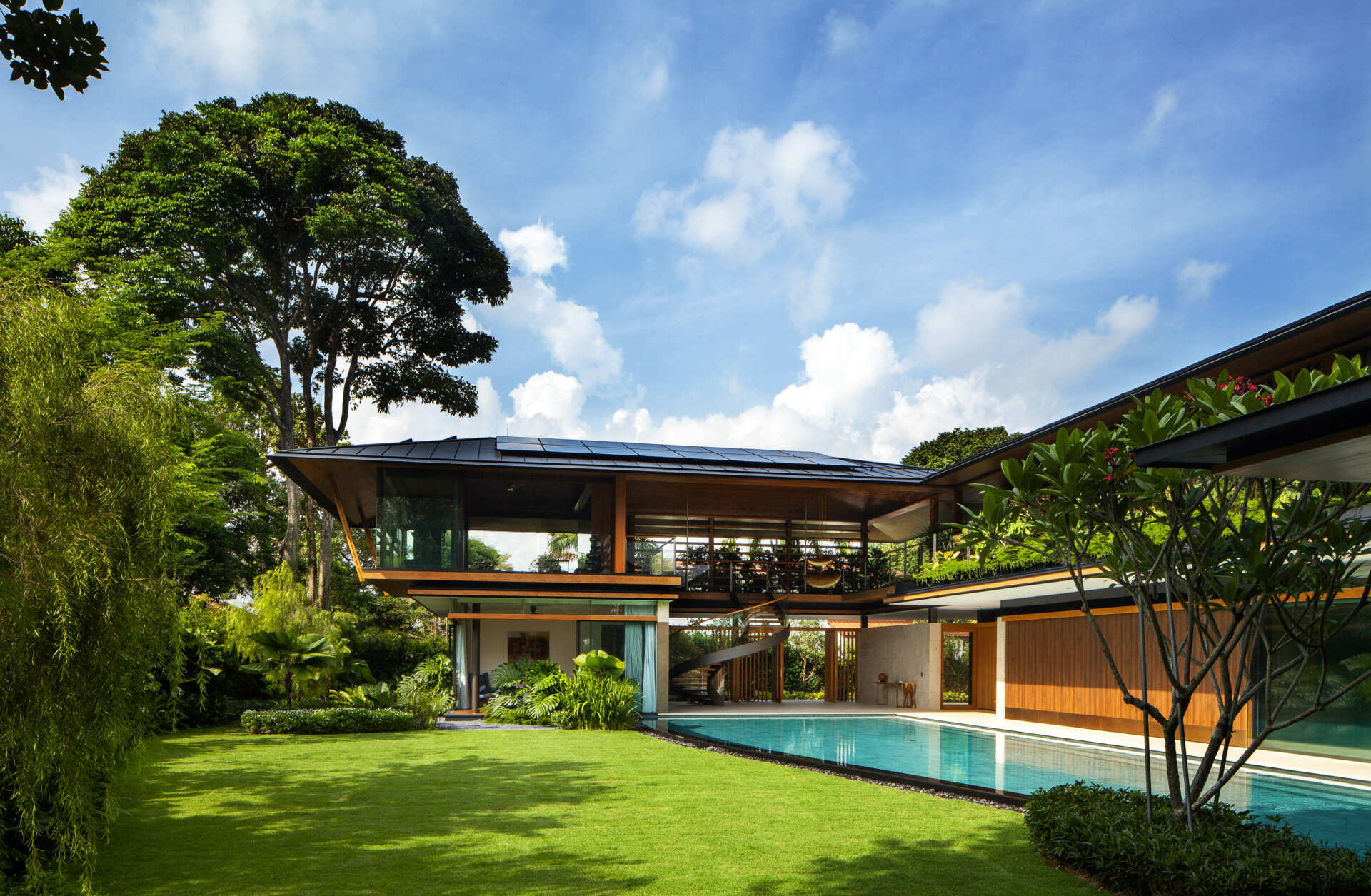 A tropical residence designed around a private courtyard garden. Featuring warm timber interiors, dramatic rooflines, a long swimming pool, lush landscaping, glass walls, and a sculptural spiral staircase, this modern home showcases the beauty of indoor-outdoor living in a tropical climate.