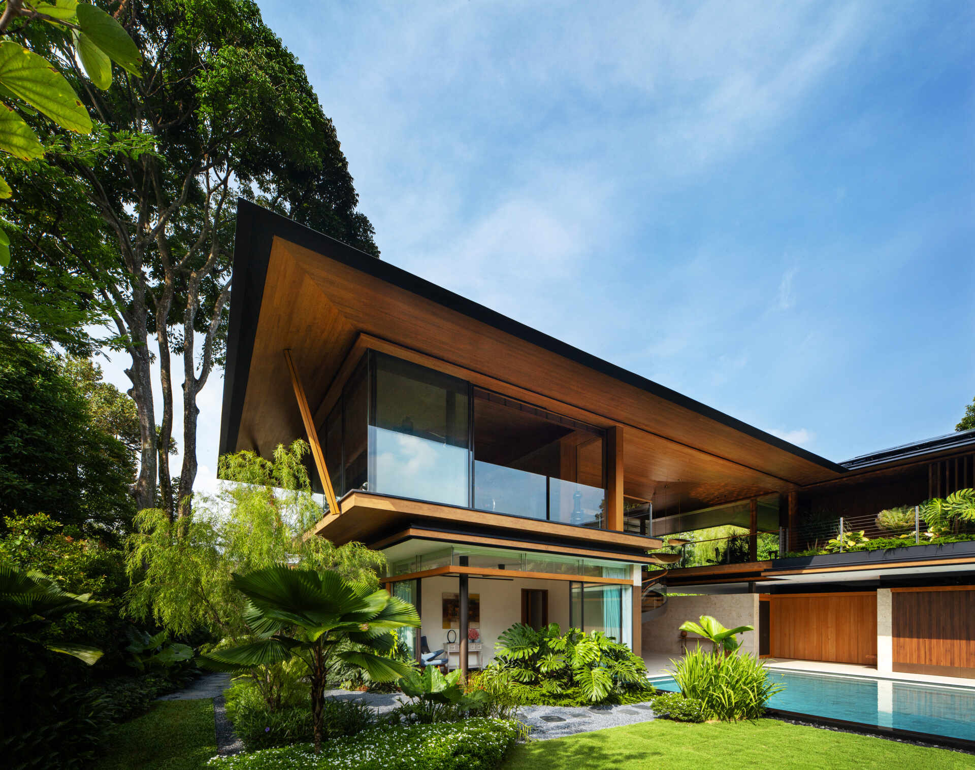 A tropical residence designed around a private courtyard garden. Featuring warm timber interiors, dramatic rooflines, a long swimming pool, lush landscaping, glass walls, and a sculptural spiral staircase, this modern home showcases the beauty of indoor-outdoor living in a tropical climate.
