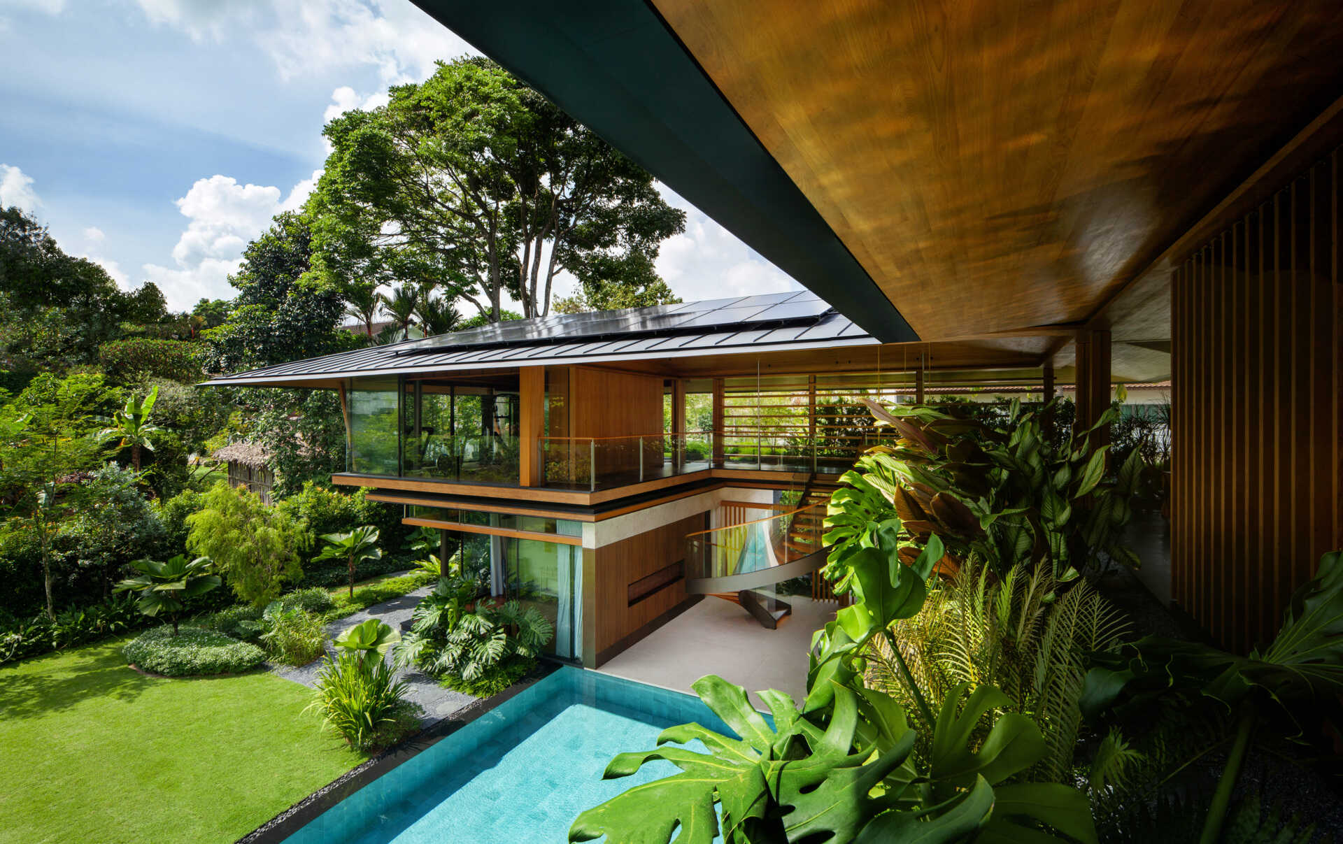 A tropical residence designed around a private courtyard garden. Featuring warm timber interiors, dramatic rooflines, a long swimming pool, lush landscaping, glass walls, and a sculptural spiral staircase, this modern home showcases the beauty of indoor-outdoor living in a tropical climate.