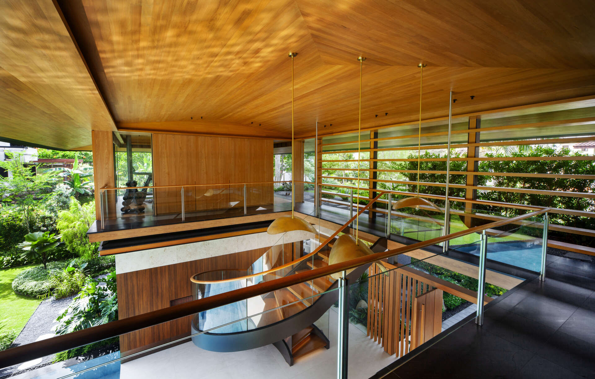 A tropical residence designed around a private courtyard garden. Featuring warm timber interiors, dramatic rooflines, a long swimming pool, lush landscaping, glass walls, and a sculptural spiral staircase, this modern home showcases the beauty of indoor-outdoor living in a tropical climate.