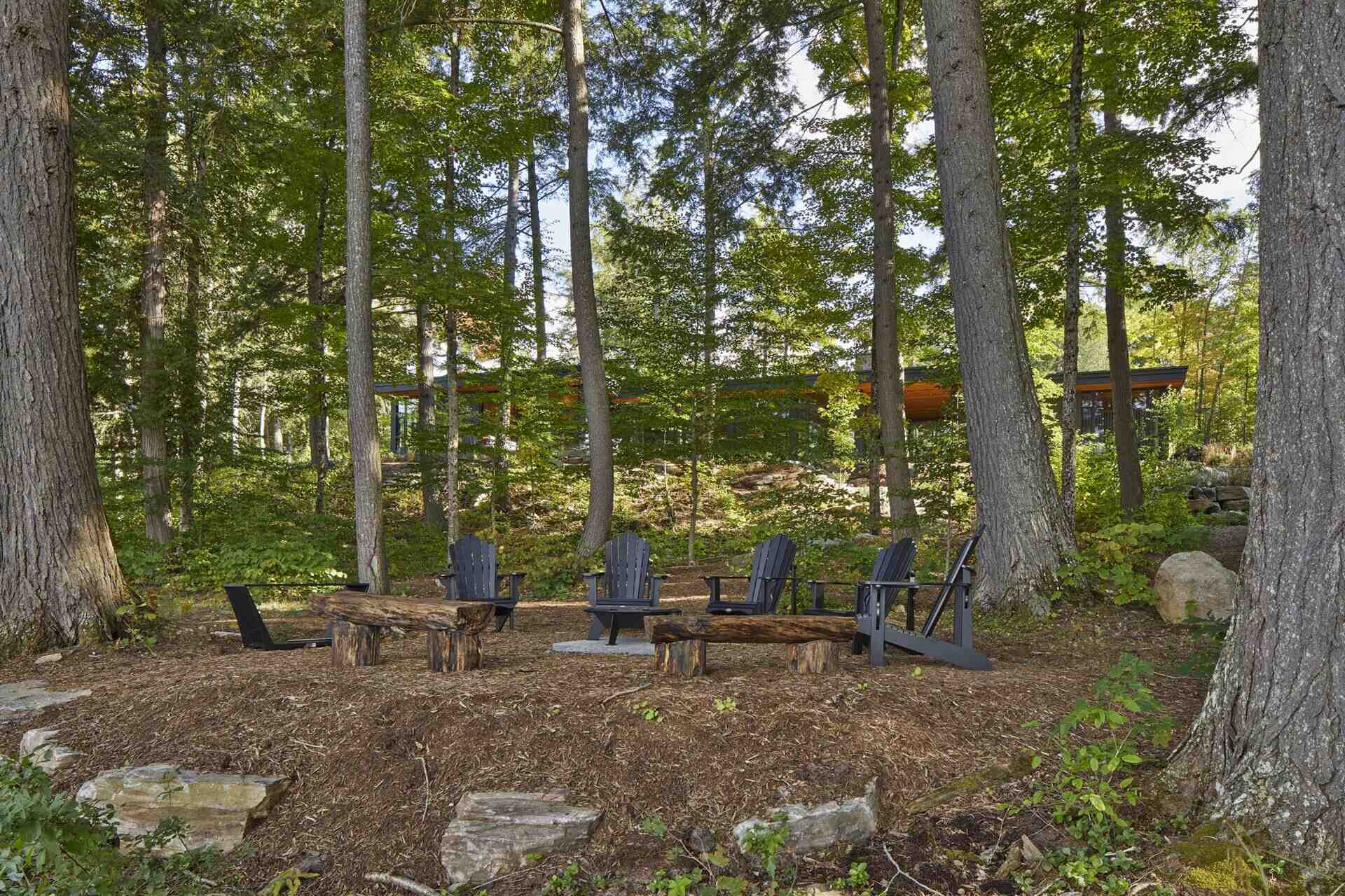 A lakeside cottage with a firepit area surrounded by seating.