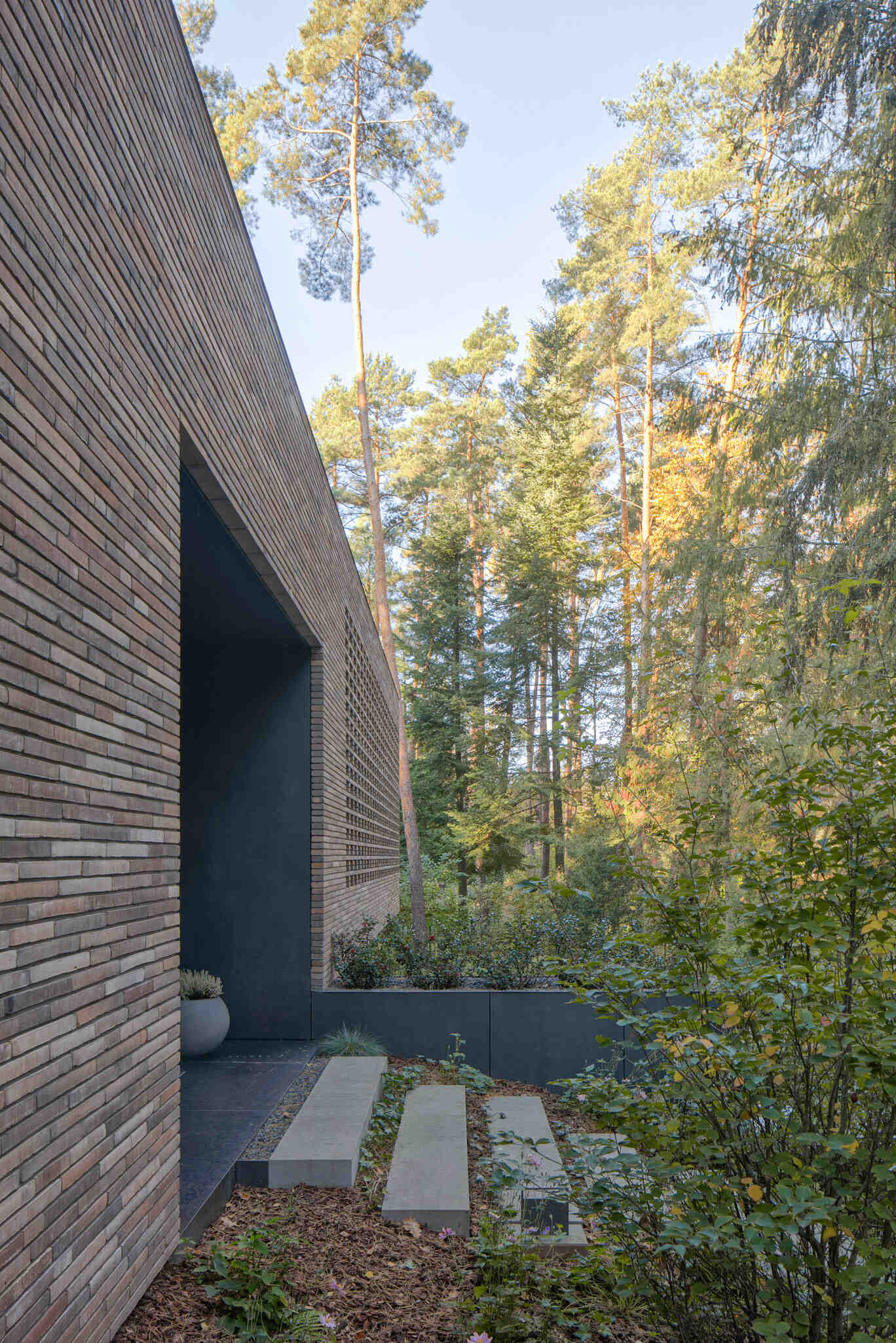 House with a Glade near Warsaw, Poland uses curved architecture, brick, glass, and graphite cladding to create a villa that seems to emerge from the surrounding pine forest.