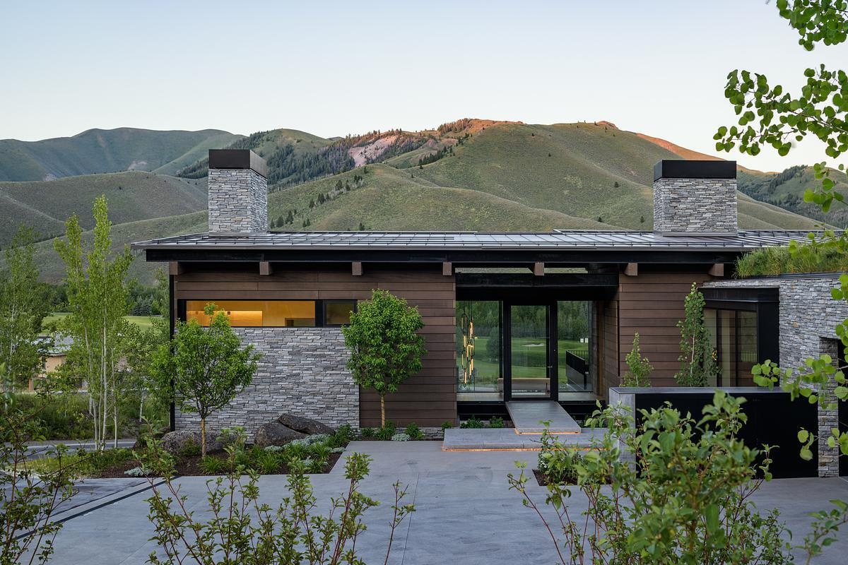 A floating bridge suspended above a dry creek bed creates a dramatic arrival experience, leading into a home defined by exposed timber, steel, stone, and breathtaking valley views.