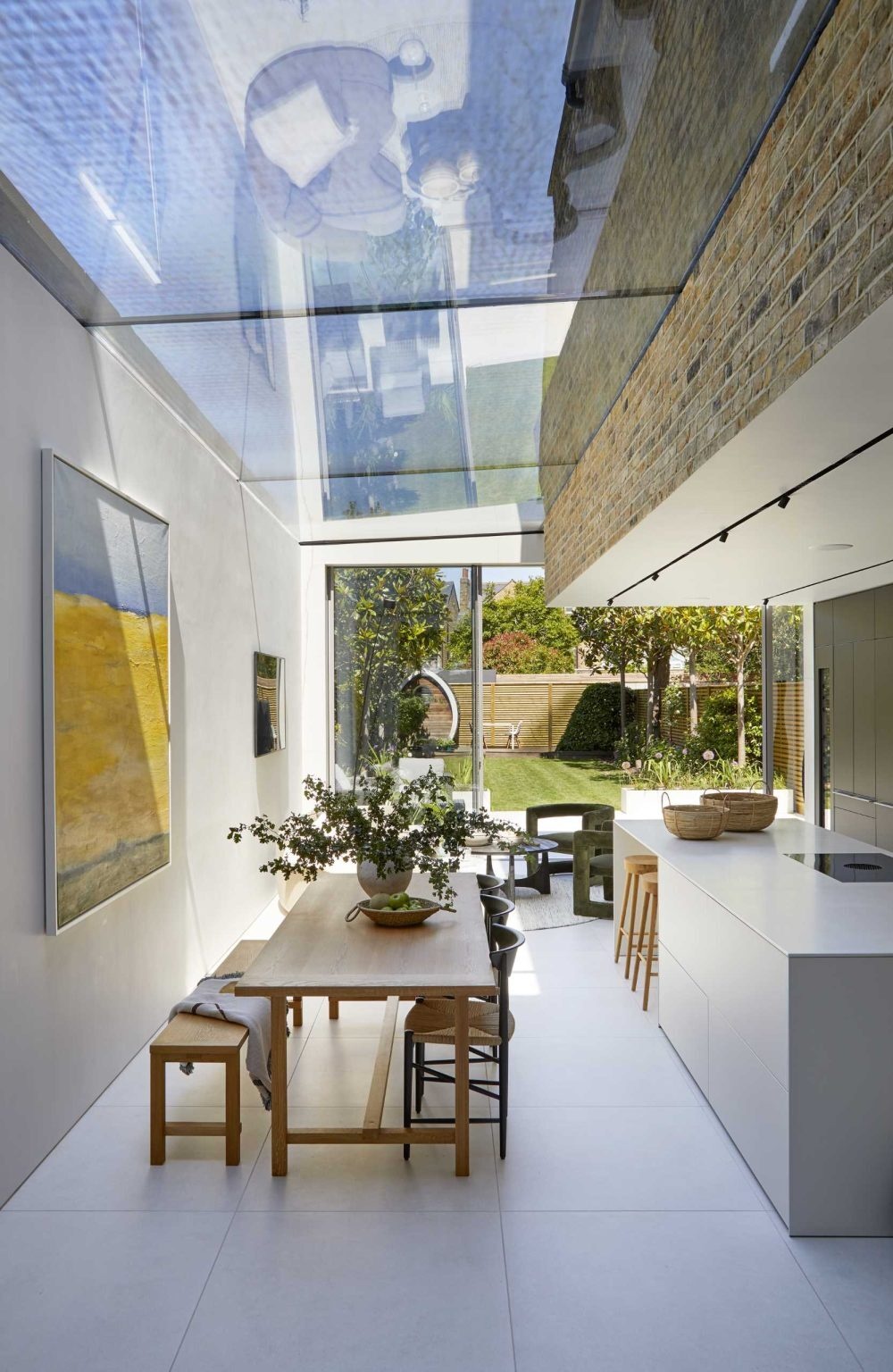 Warm timber furnishings, contemporary details, and colorful artwork create an inviting dining area beneath a skylight.