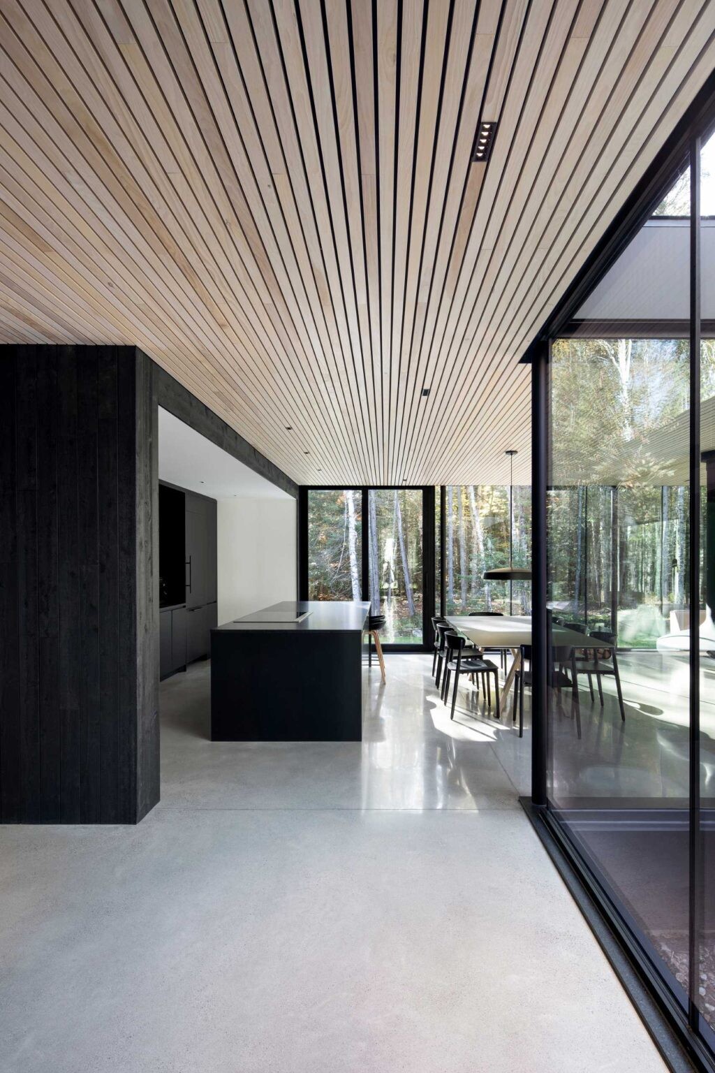 A minimalist kitchen with black cabinetry and a central island opens toward the dining and living areas in a continuous floor plan.