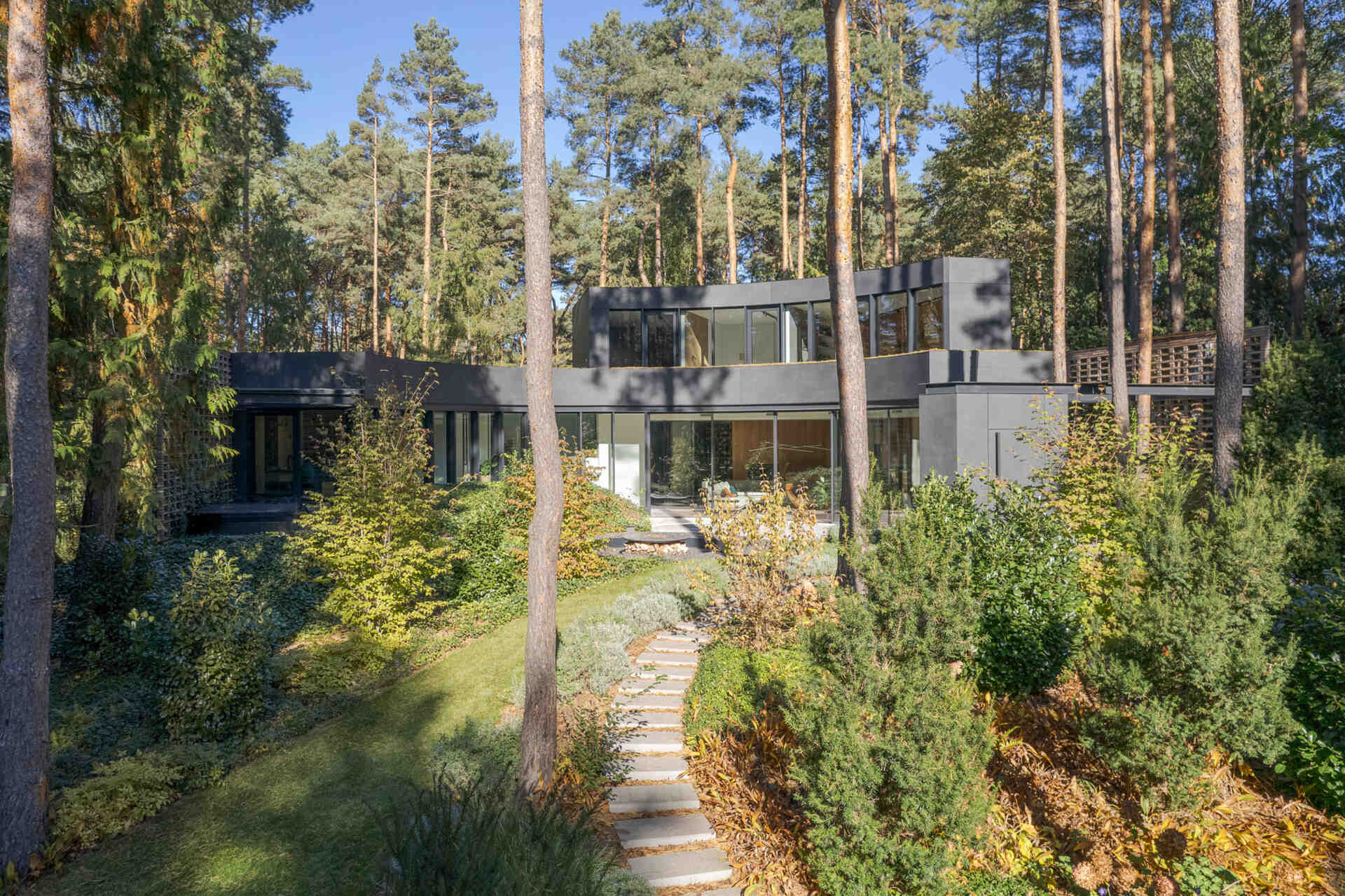 This forest villa near Warsaw uses landscaping as part of the architecture. Existing pines, filtered sunlight, and matching indoor-outdoor flooring patterns help create a seamless experience between house and garden.