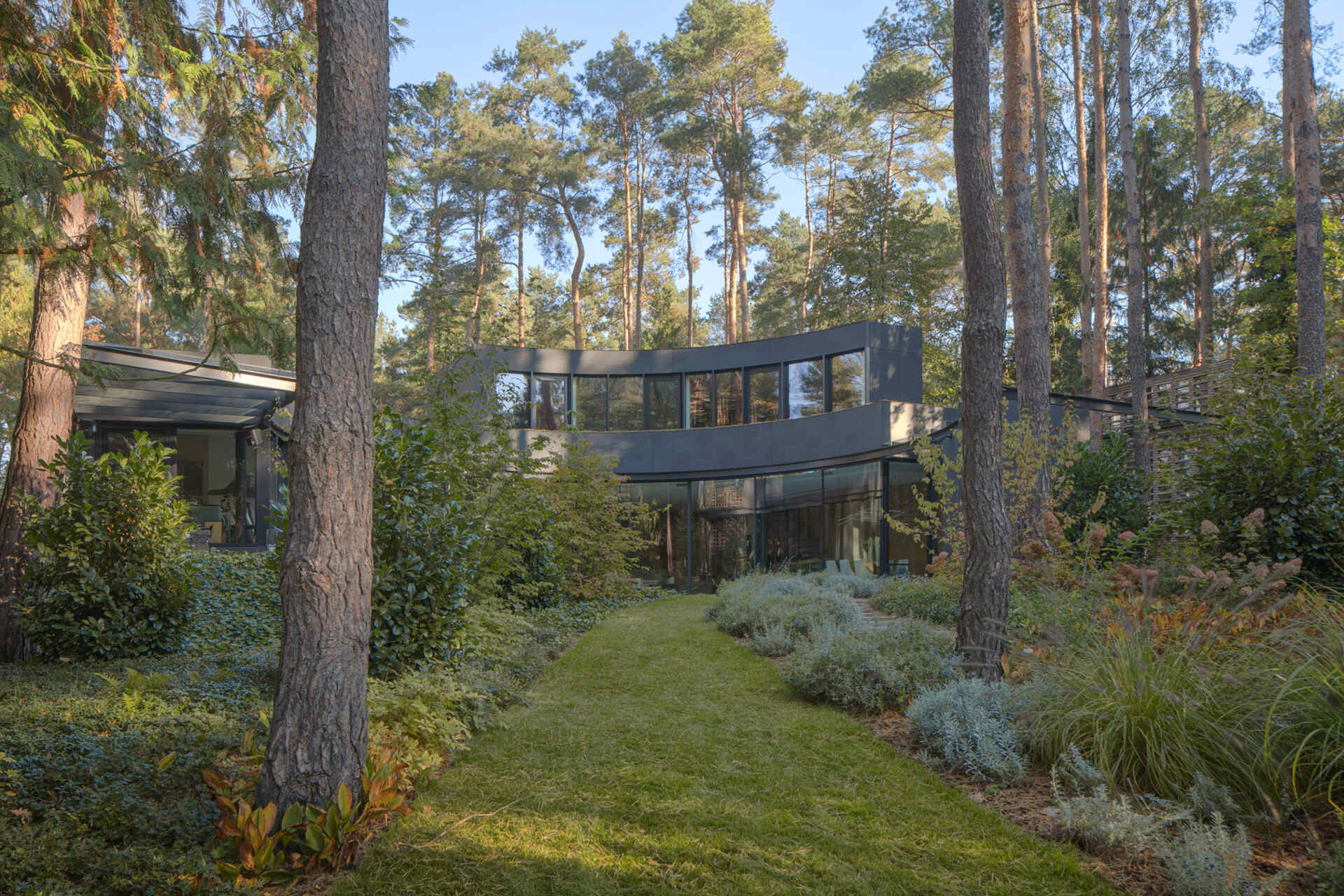 This forest villa near Warsaw uses landscaping as part of the architecture. Existing pines, filtered sunlight, and matching indoor-outdoor flooring patterns help create a seamless experience between house and garden.