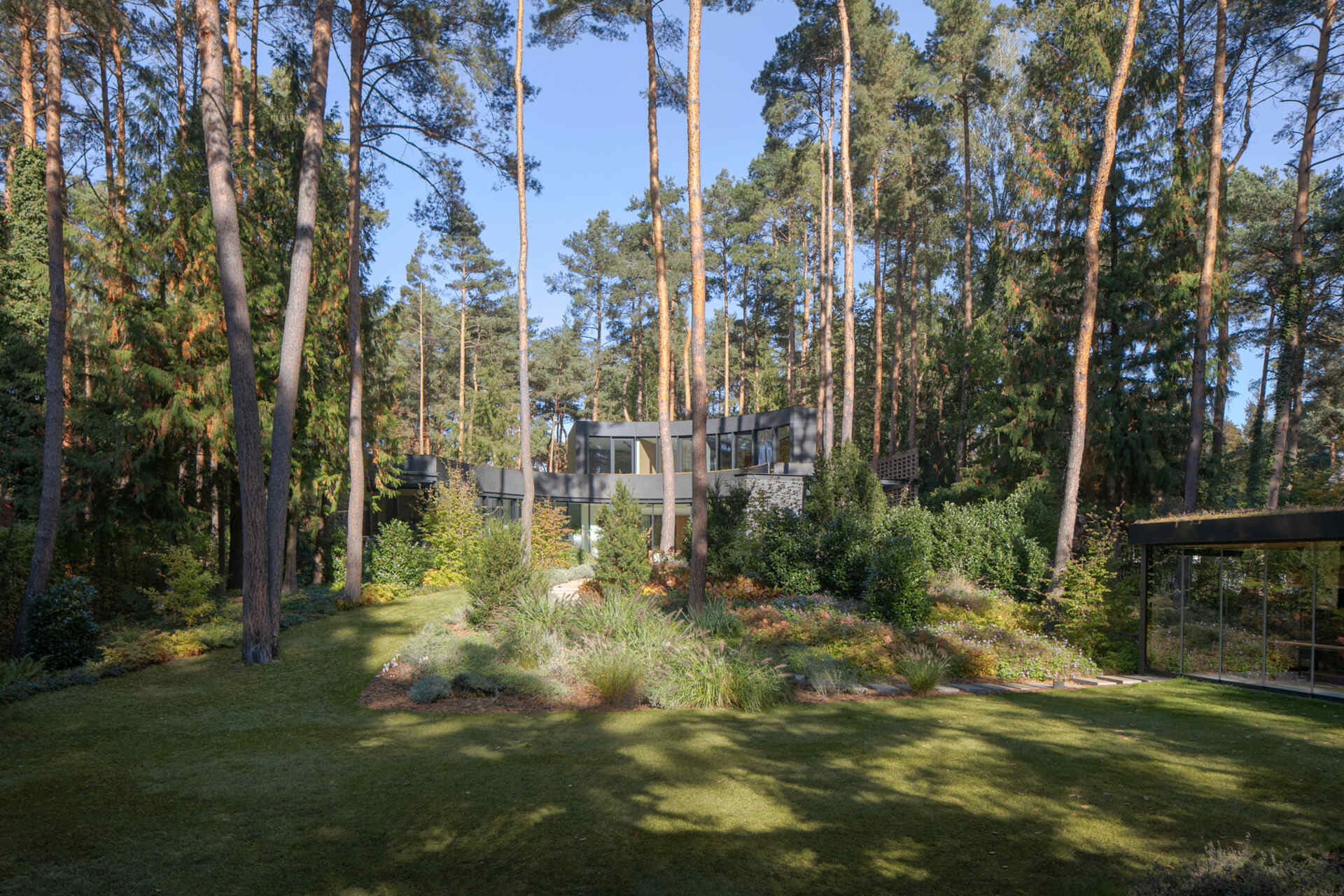 This forest villa near Warsaw uses landscaping as part of the architecture. Existing pines, filtered sunlight, and matching indoor-outdoor flooring patterns help create a seamless experience between house and garden.