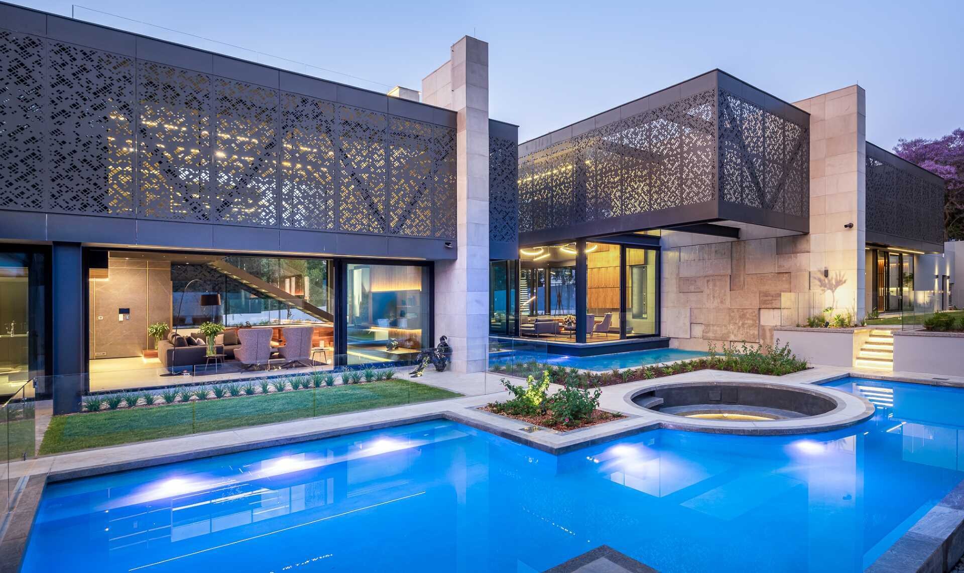 Perforated aluminum screens, water features, sculpture, and hidden lighting combine to create a dramatic entrance to this modern Johannesburg home.