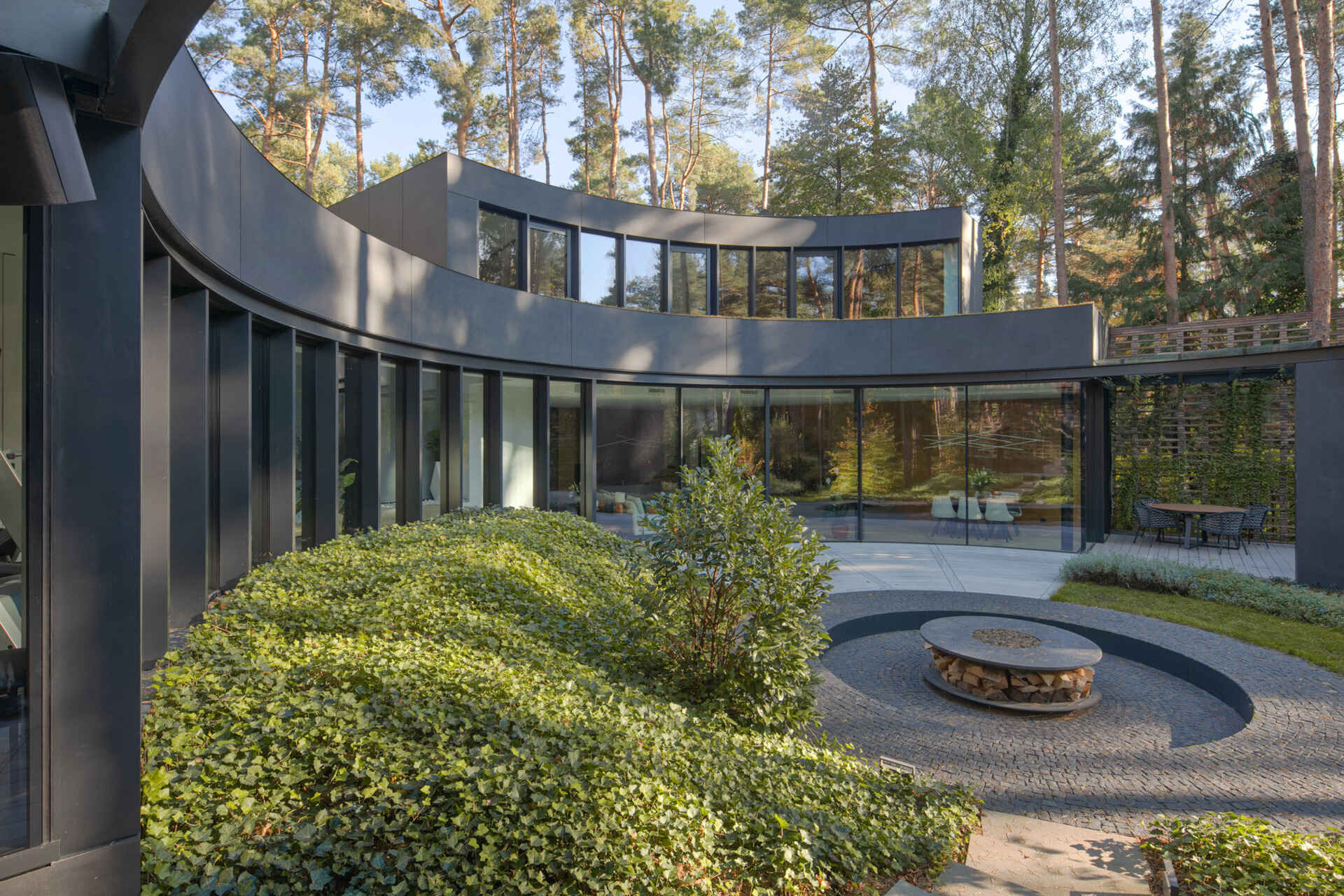House with a Glade near Warsaw, Poland uses curved architecture, brick, glass, and graphite cladding to create a villa that seems to emerge from the surrounding pine forest.