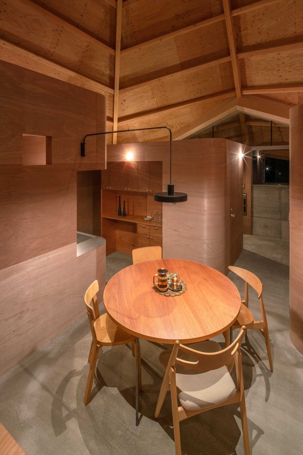 A compact kitchen with contrasting wood finishes brings warmth and character to this open-plan Japanese home while maintaining a seamless connection to surrounding spaces.