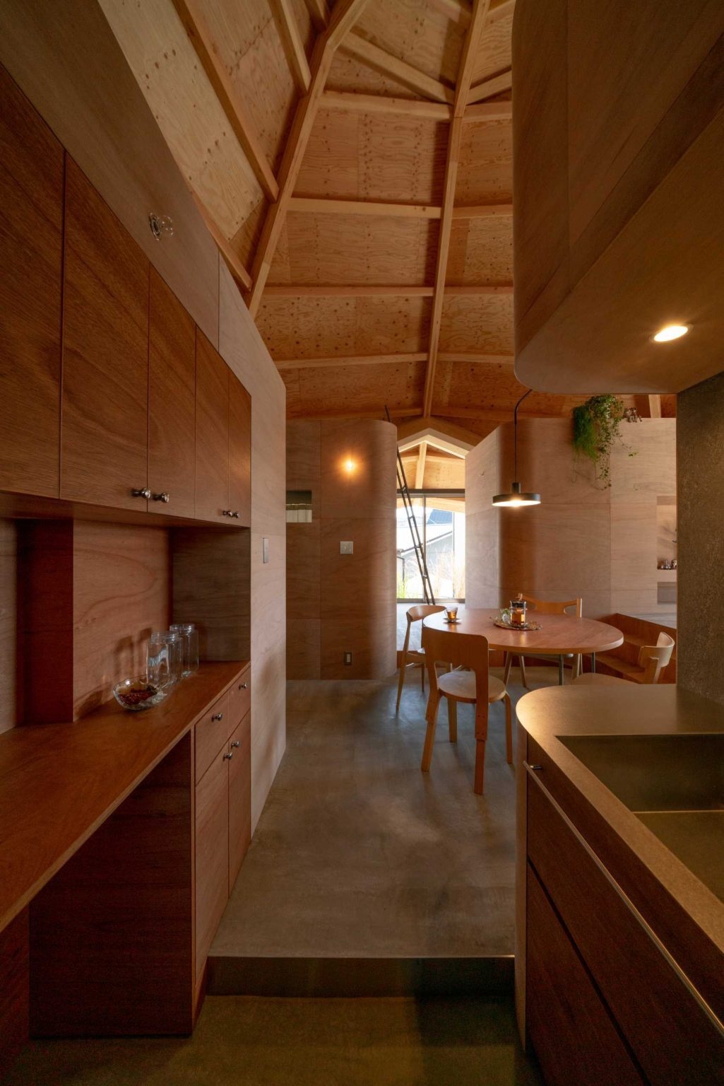 A compact kitchen with contrasting wood finishes brings warmth and character to this open-plan Japanese home while maintaining a seamless connection to surrounding spaces.