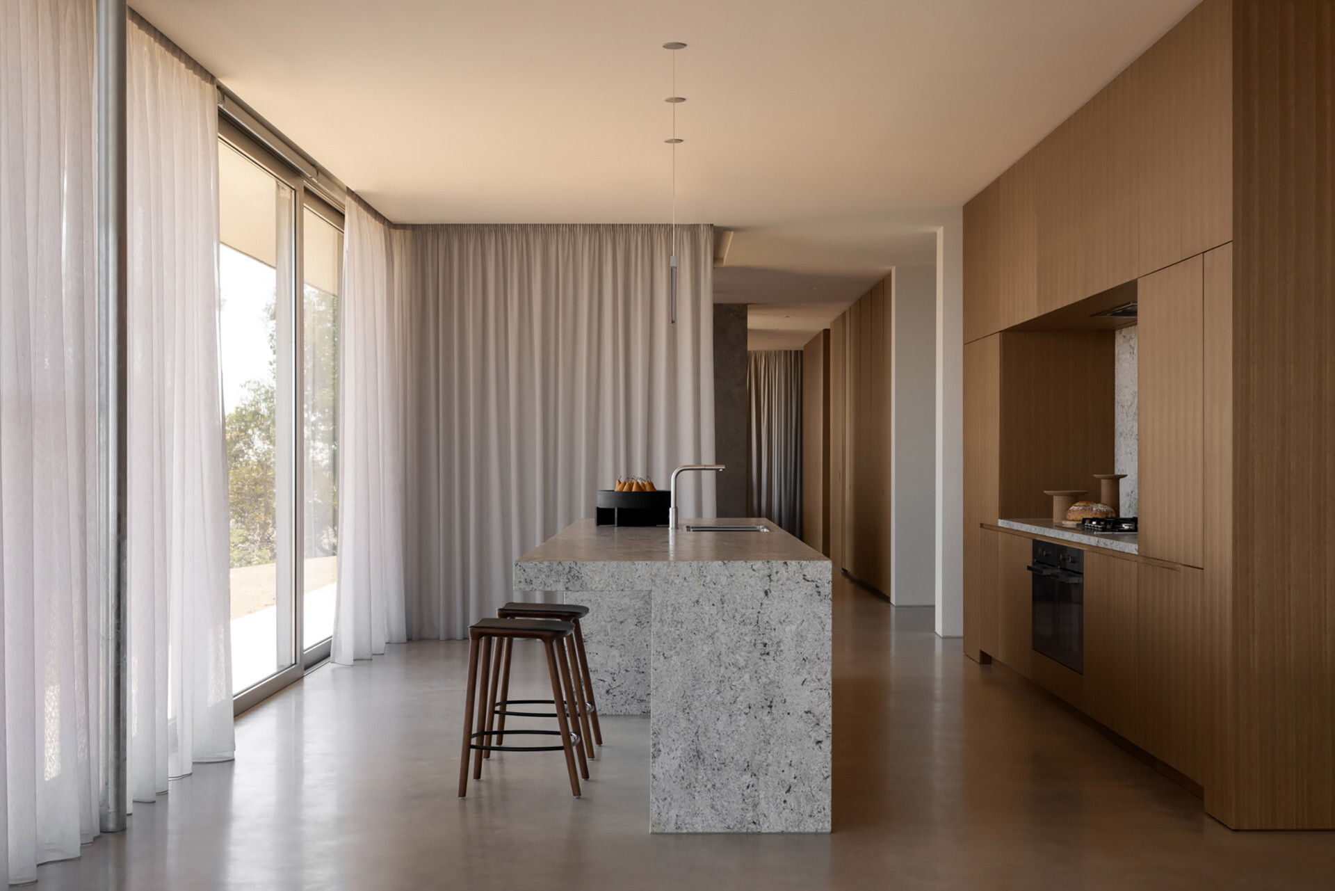 Natural stone surfaces, integrated storage, and warm-toned joinery define a minimalist kitchen designed for both function and entertaining.