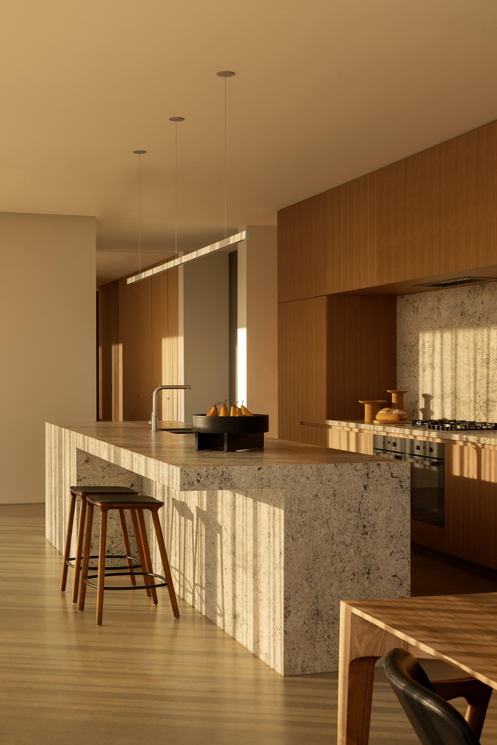 Natural stone surfaces, integrated storage, and warm-toned joinery define a minimalist kitchen designed for both function and entertaining.
