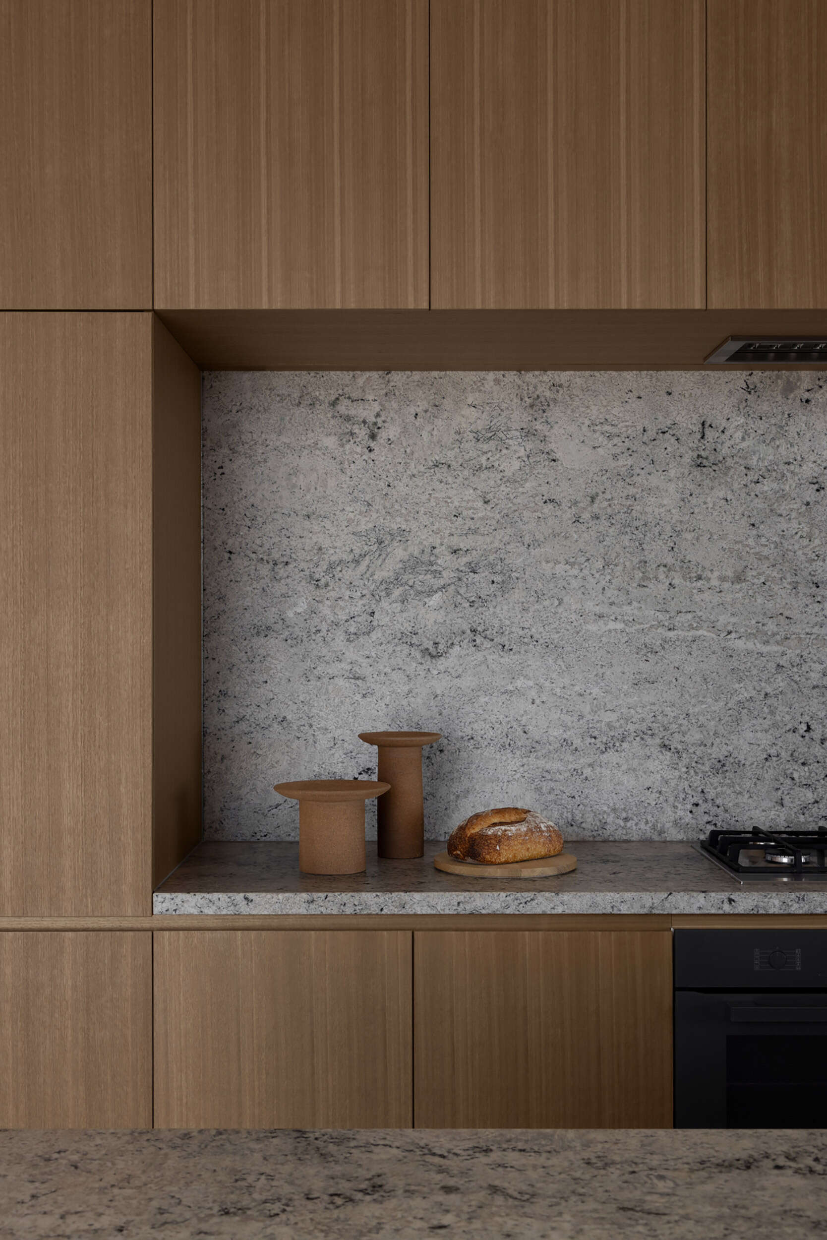 Natural stone surfaces, integrated storage, and warm-toned joinery define a minimalist kitchen designed for both function and entertaining.