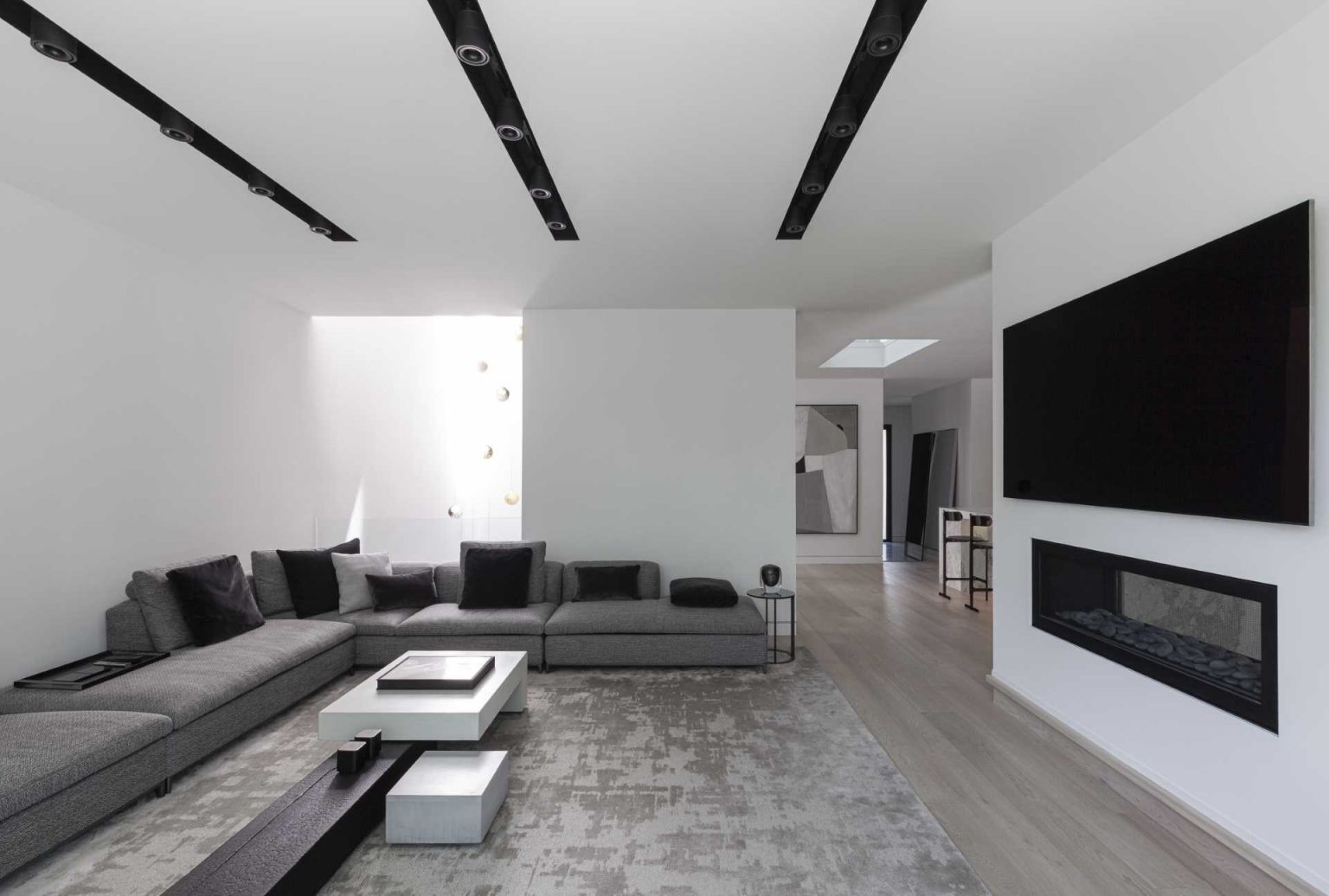 Inside Stack House, multiple living areas offer different experiences, from a bookshelf-lined lounge to a cozy fireplace setting. The flowing layout creates visual connections throughout the home.
