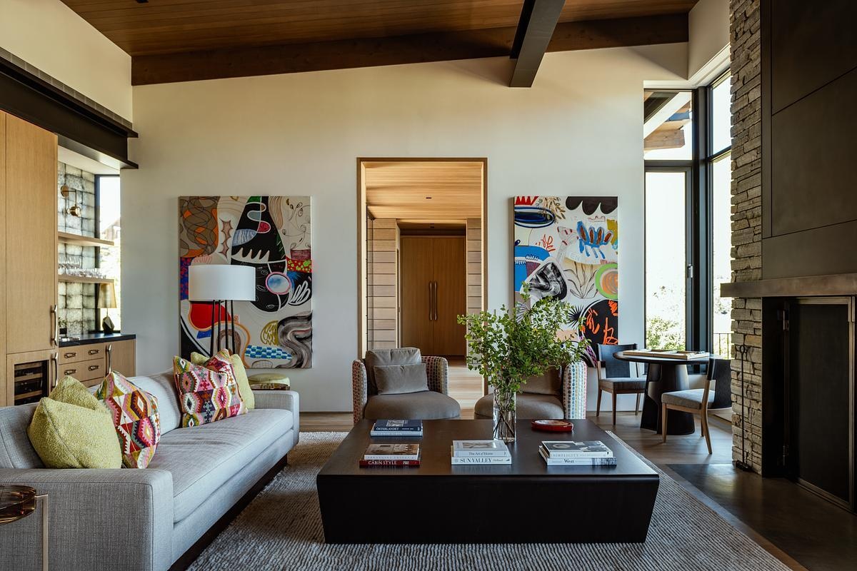 Vaulted ceilings, exposed timber beams, stone walls, and floor-to-ceiling glass create a stunning great room where mountain views become part of the interior design.