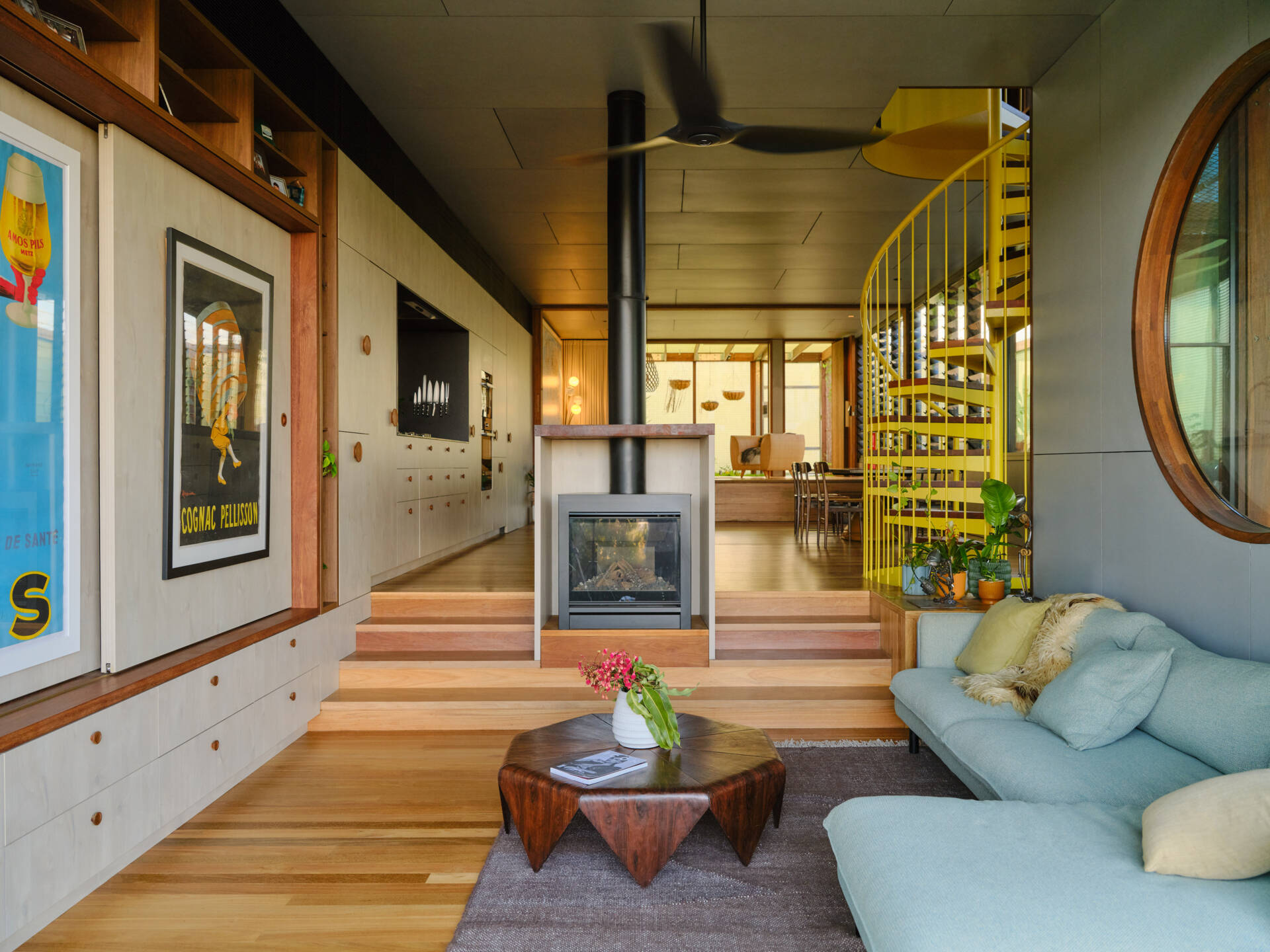 Custom timber cabinetry, a wood stove, and a dramatic circular window bring warmth and personality to this modern living room.