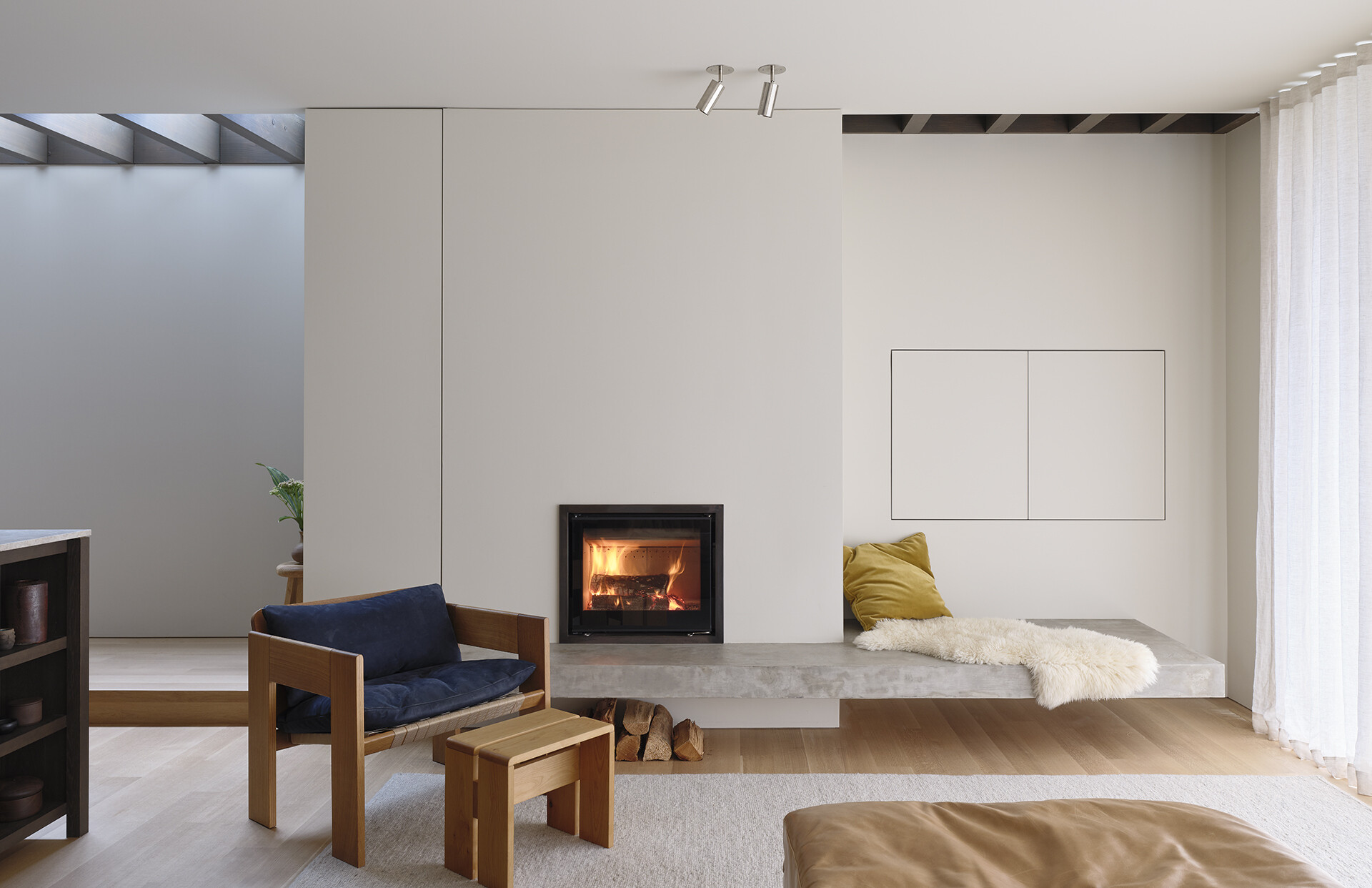 A concrete fireplace hearth becomes built-in seating in this bright living room filled with natural light and garden views.