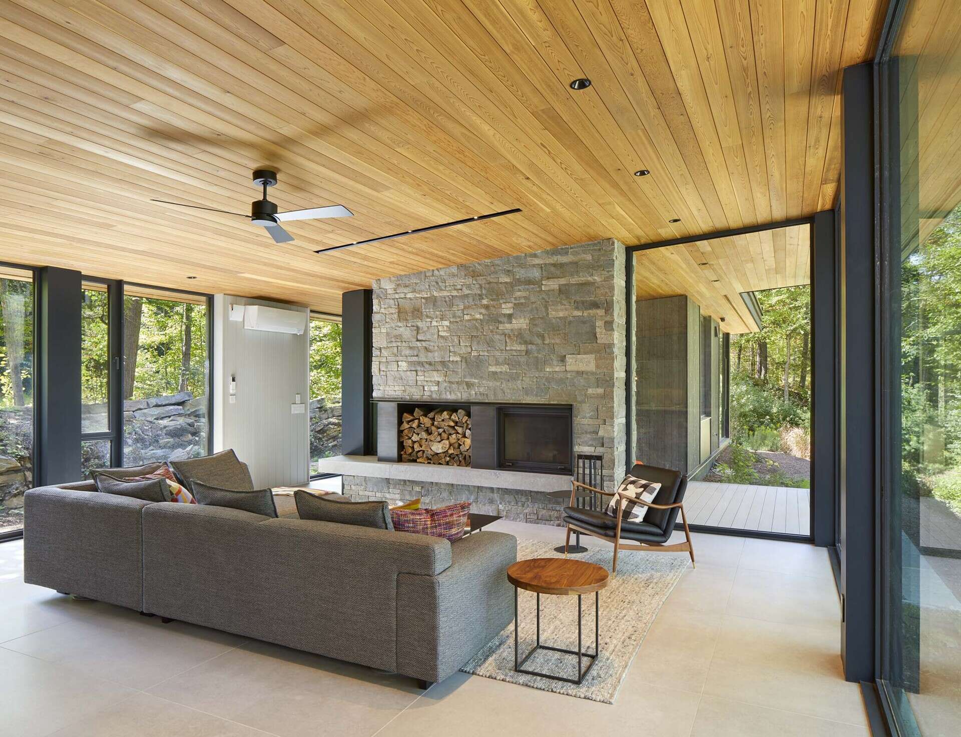 The central great room contains the living space and is defined by expansive floor-to-ceiling glazing that frames views across Percy Lake. A blackened-steel wood-burning fireplace with a stone surround, anchors the room and acts as a focal point within the open space.