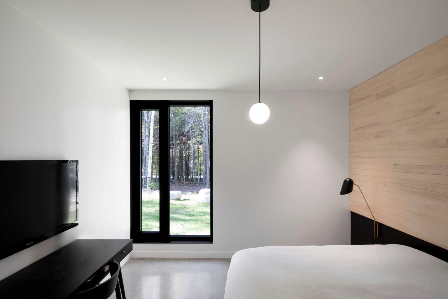 A bedroom with a wood accent wall and minimal furniture creates a calm space that continues the home’s natural material palette.