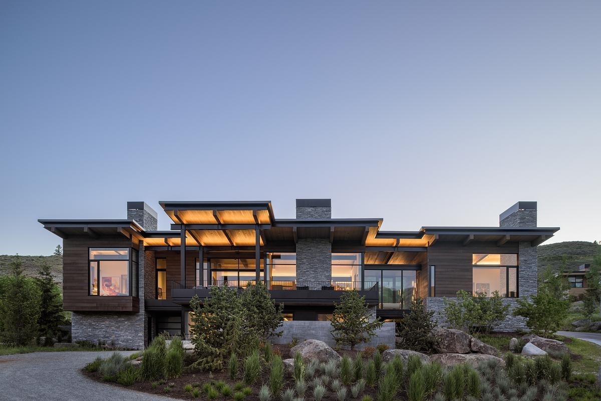 This modern mountain home blends into an Idaho hillside with a living green roof, Oakley stone walls, Douglas fir siding, and expansive glazing that frames mountain views while softening its presence on the landscape.