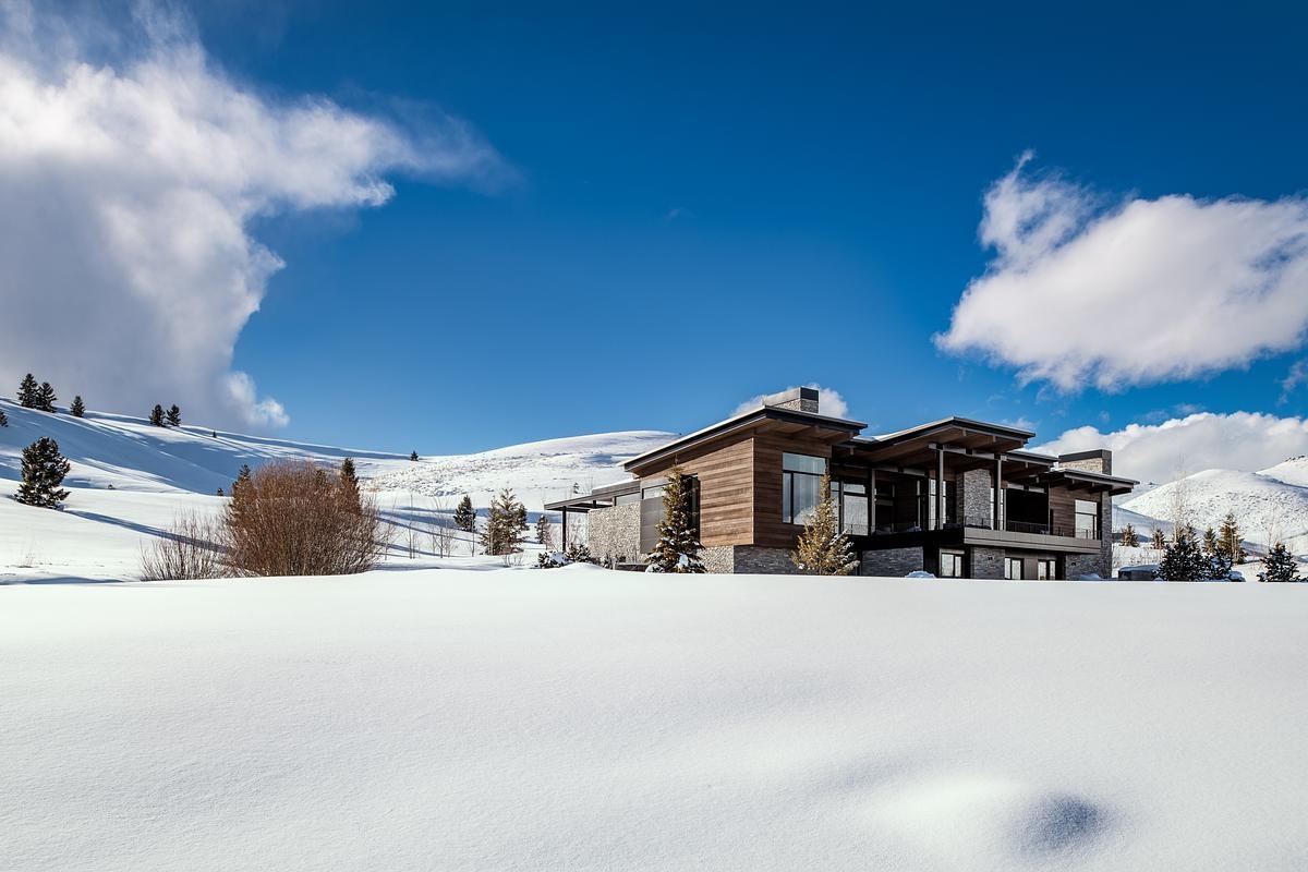 This modern mountain home blends into an Idaho hillside with a living green roof, Oakley stone walls, Douglas fir siding, and expansive glazing that frames mountain views while softening its presence on the landscape.