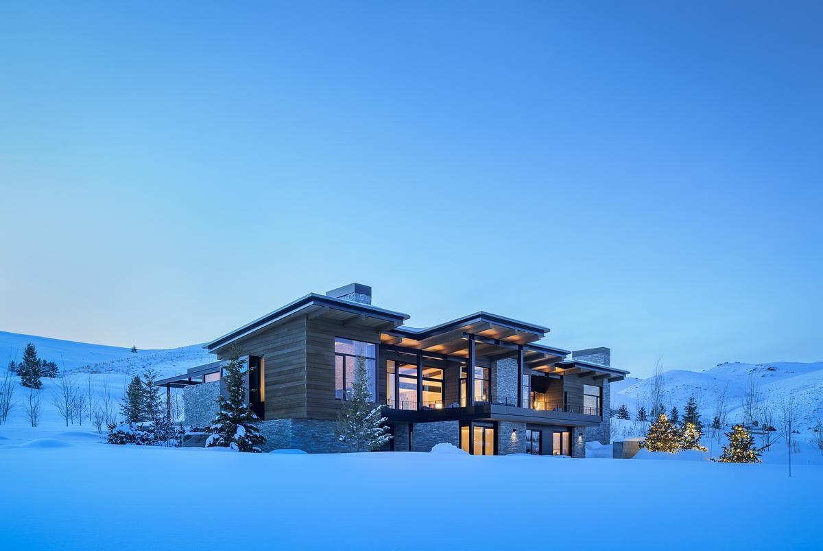This modern mountain home blends into an Idaho hillside with a living green roof, Oakley stone walls, Douglas fir siding, and expansive glazing that frames mountain views while softening its presence on the landscape.