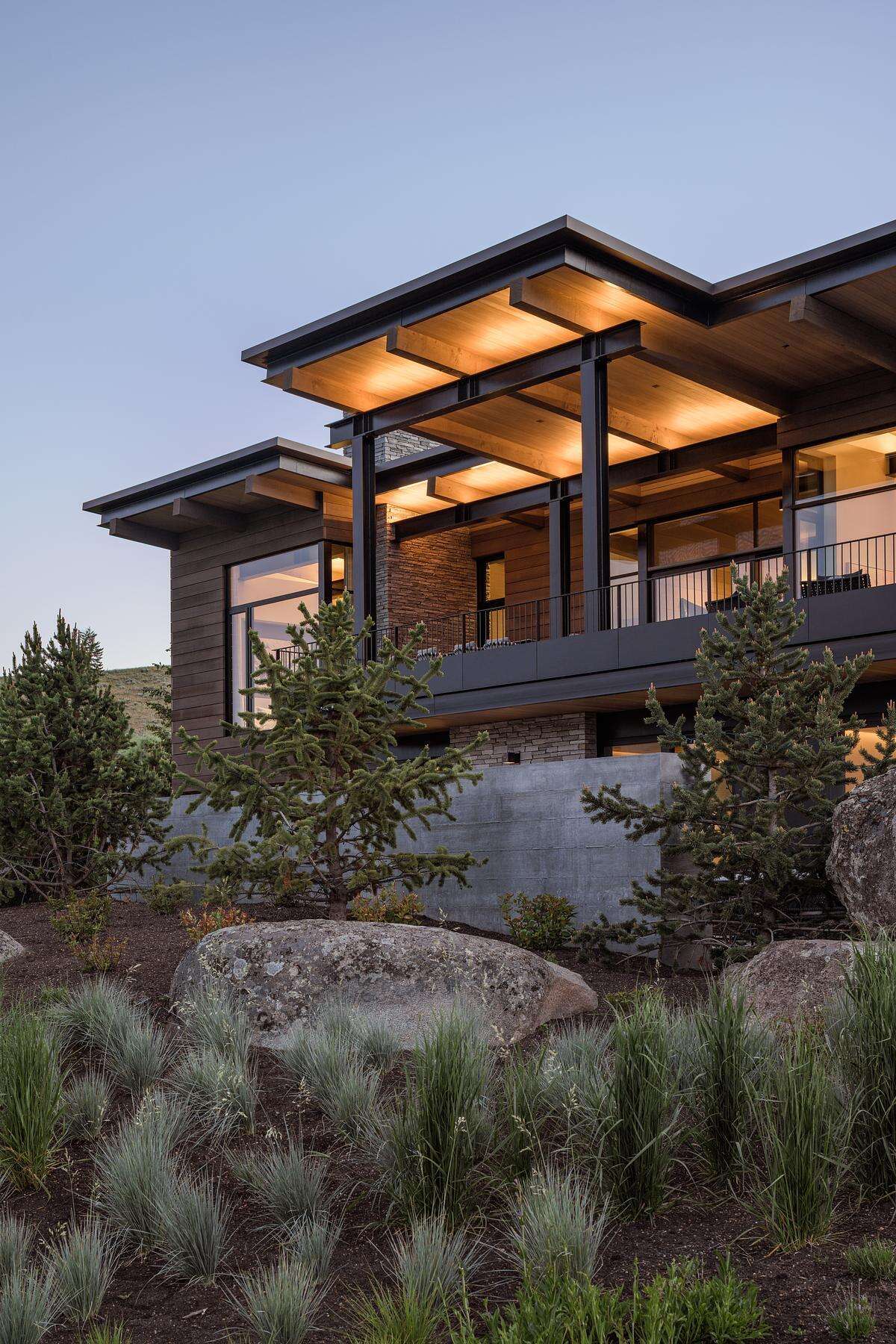 This modern mountain home blends into an Idaho hillside with a living green roof, Oakley stone walls, Douglas fir siding, and expansive glazing that frames mountain views while softening its presence on the landscape.