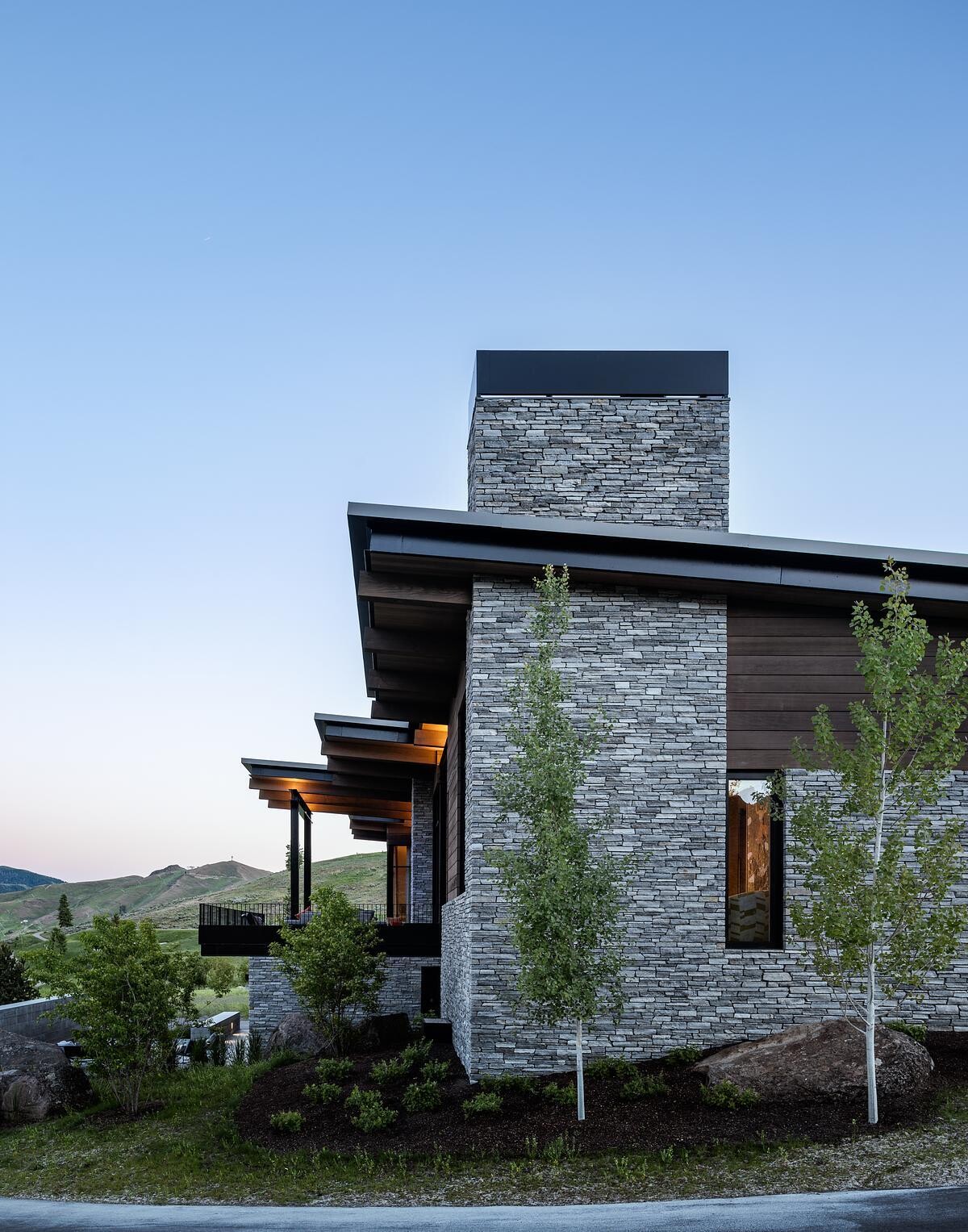 This modern mountain home blends into an Idaho hillside with a living green roof, Oakley stone walls, Douglas fir siding, and expansive glazing that frames mountain views while softening its presence on the landscape.