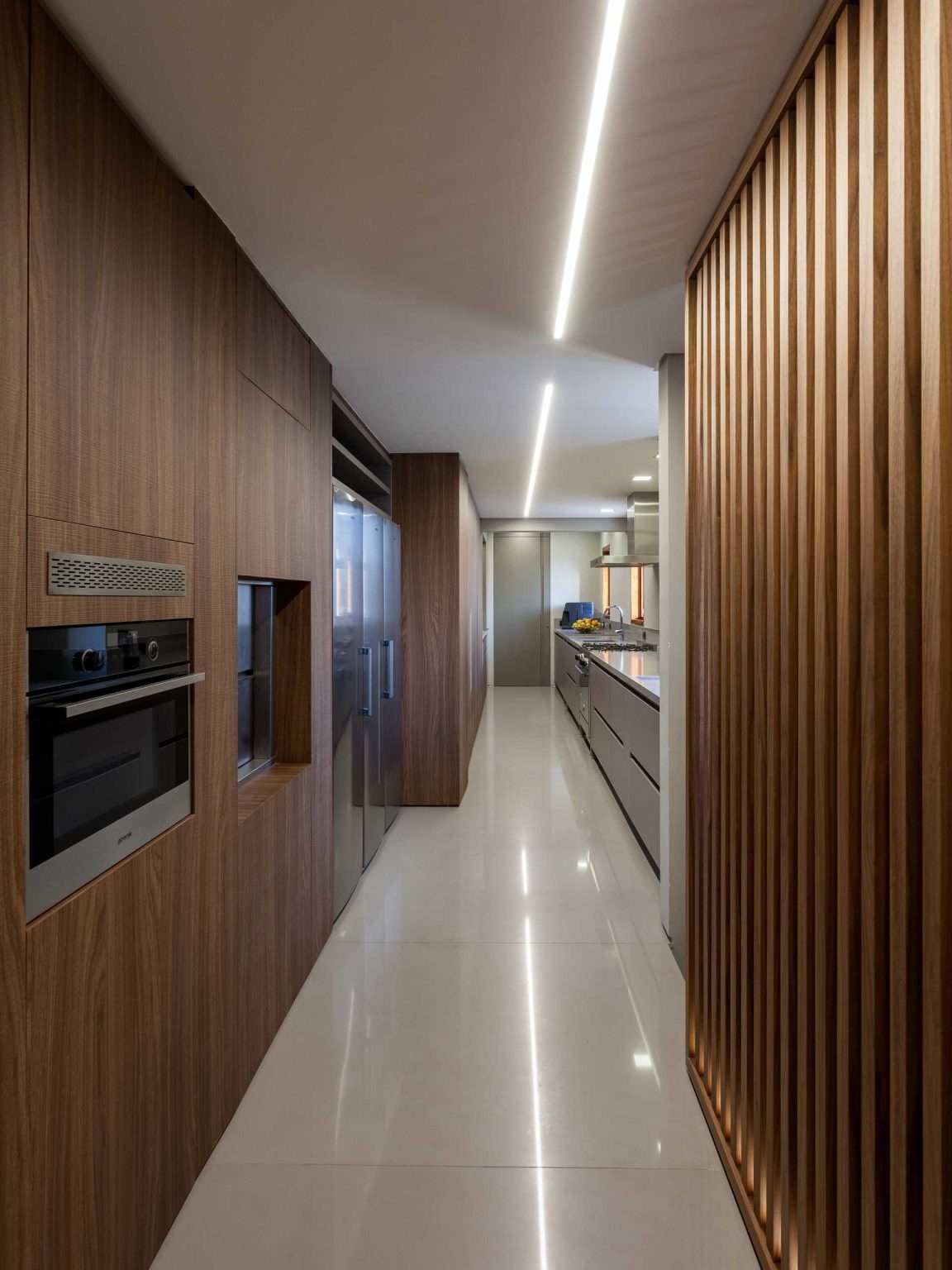 This long contemporary kitchen combines luxury finishes with practical planning. A clever pass-through window links the kitchen, pantry, and dining room for seamless entertaining.