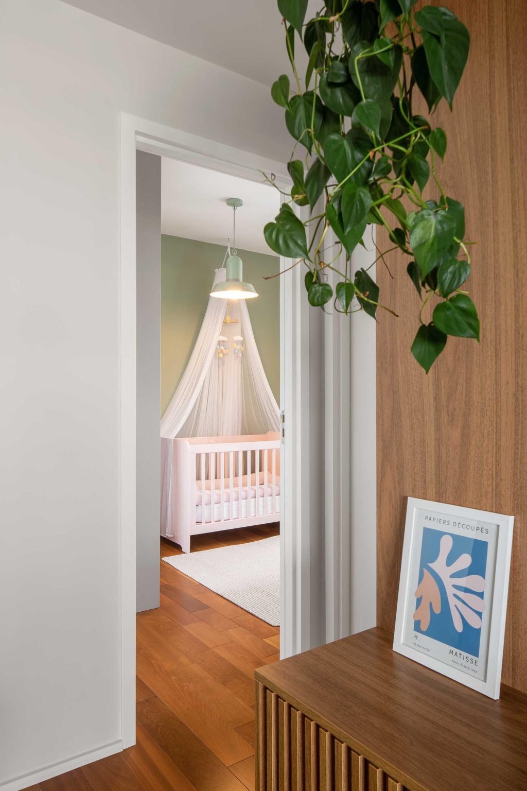 Soft green walls and a pale pink crib create a charming nursery filled with gentle color and a welcoming atmosphere.