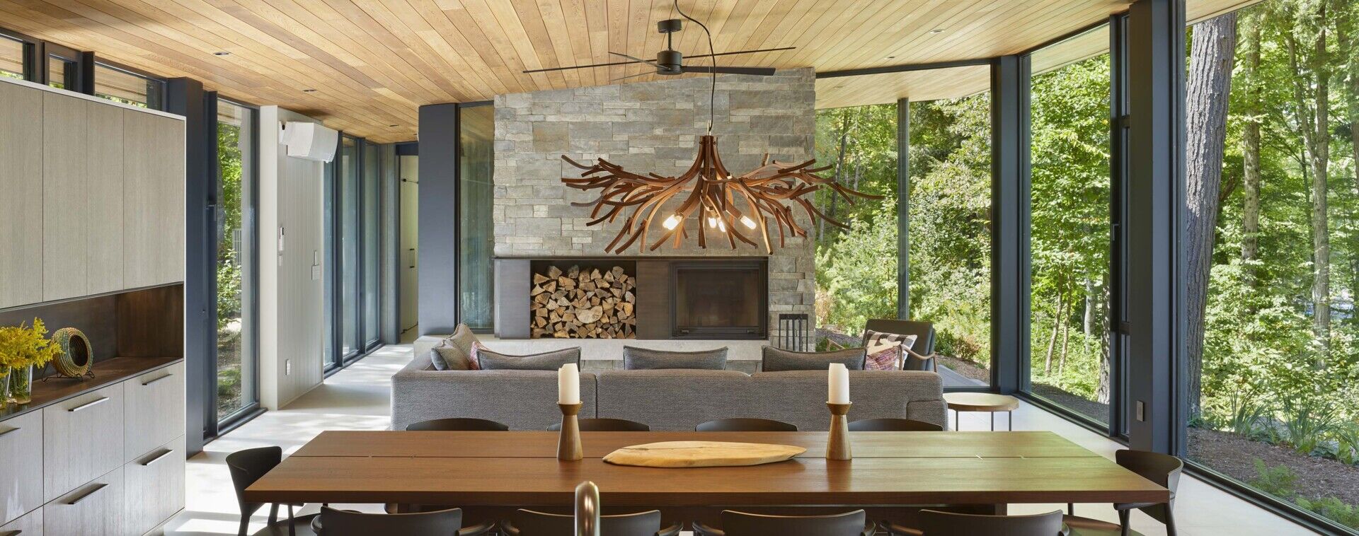 The dining area is located within the central great room and sits beside the lake-facing floor-to-ceiling windows. A custom solid walnut dining table is positioned within this space, accompanied by a chandelier made from recycled wood by Toronto makers The Brothers Dressler.