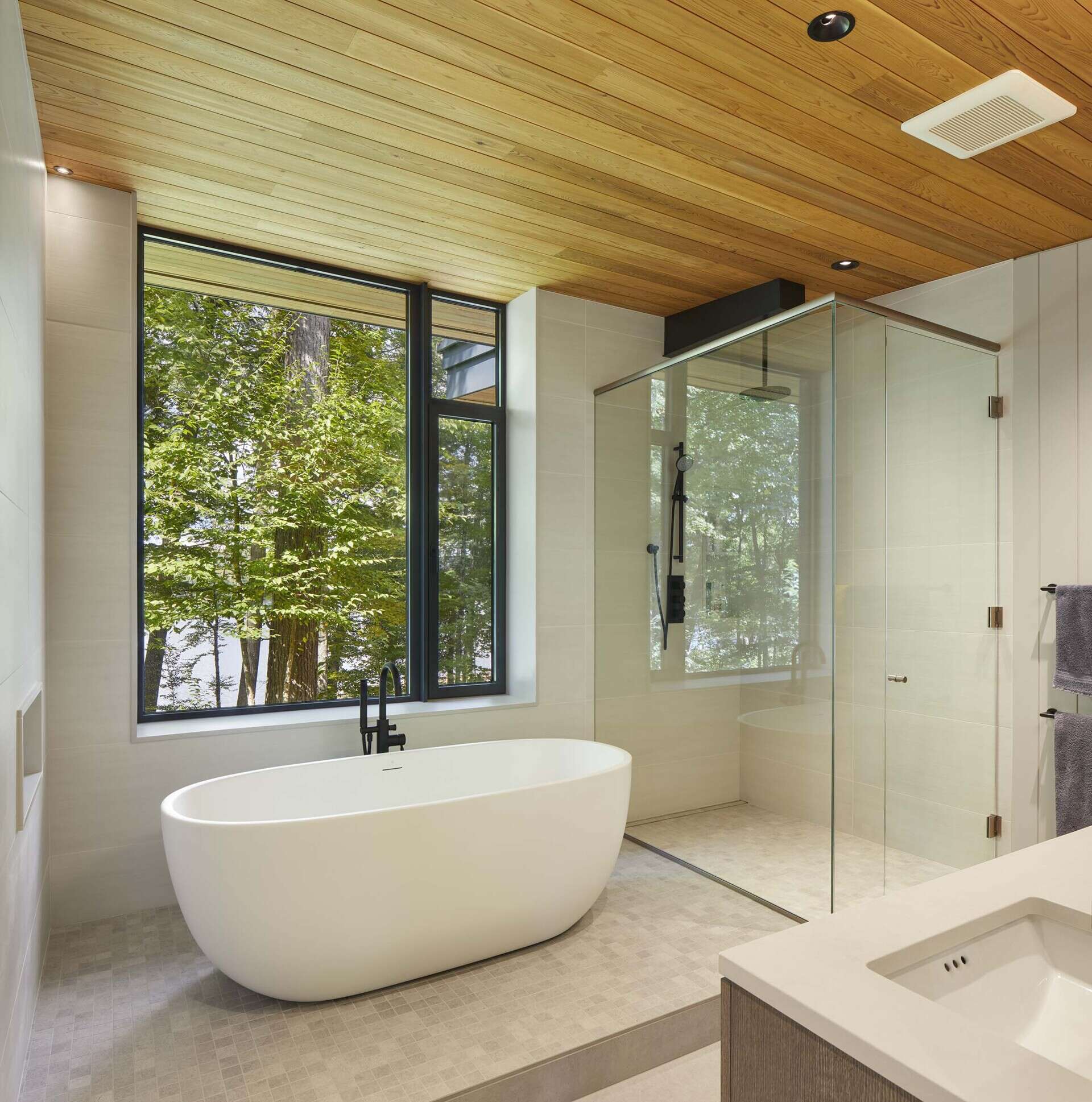 In the bathroom, a freestanding tub, glass shower, soft neutral tile, and matte black fixtures create a calm, modern place to unwind.