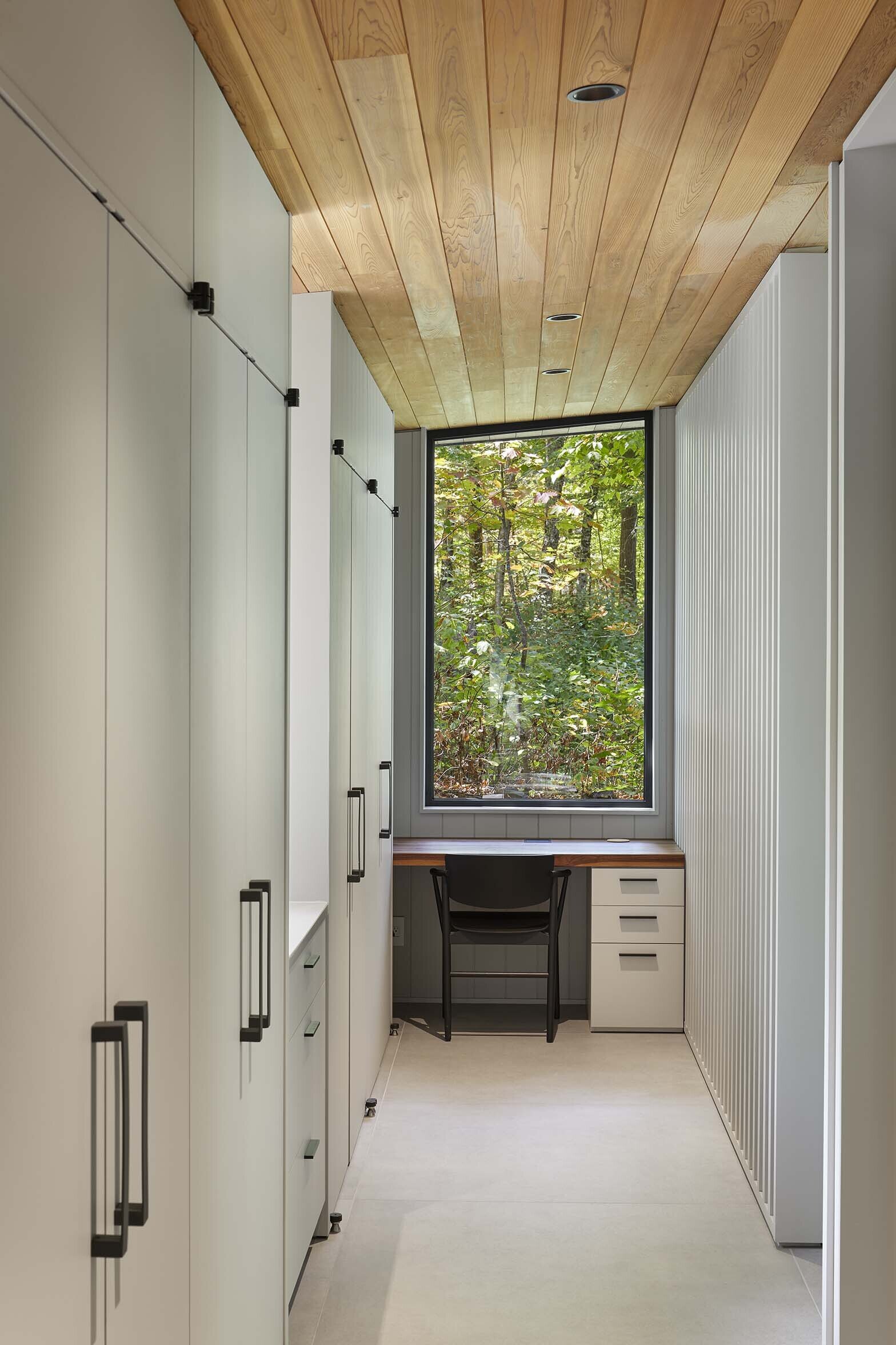 In this primary bedroom suite, closets line the wall, a desk sits beneath a window, and a partition becomes a backdrop for the bed.