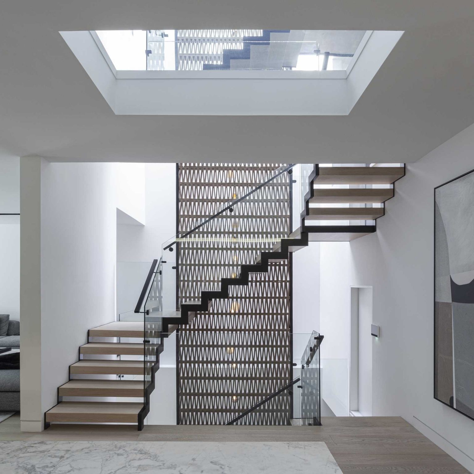 A dramatic quadruple-height staircase runs through the center of Stack House, drawing natural light from skylights above down to the basement while linking every level of the home.