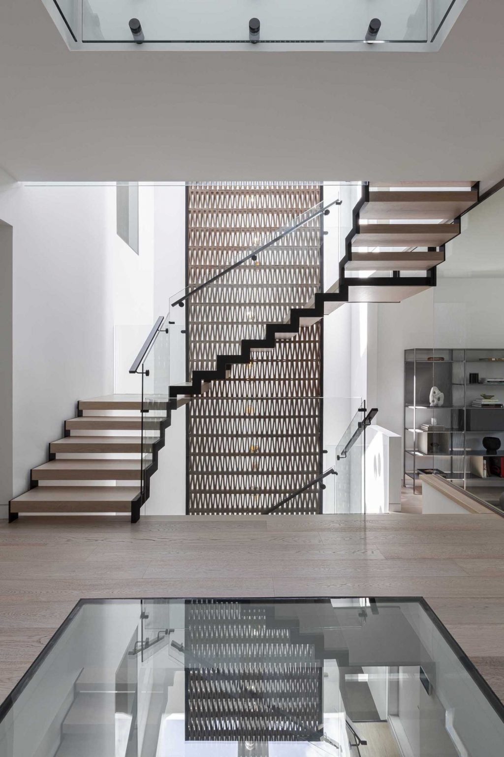 A dramatic quadruple-height staircase runs through the center of Stack House, drawing natural light from skylights above down to the basement while linking every level of the home.