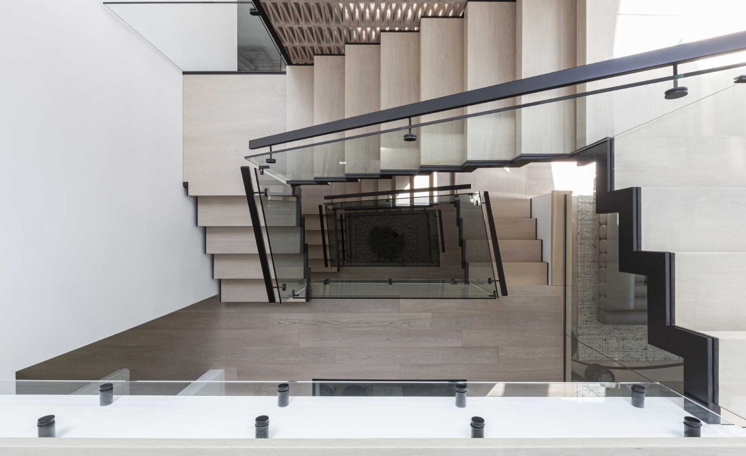 A dramatic quadruple-height staircase runs through the center of Stack House, drawing natural light from skylights above down to the basement while linking every level of the home.