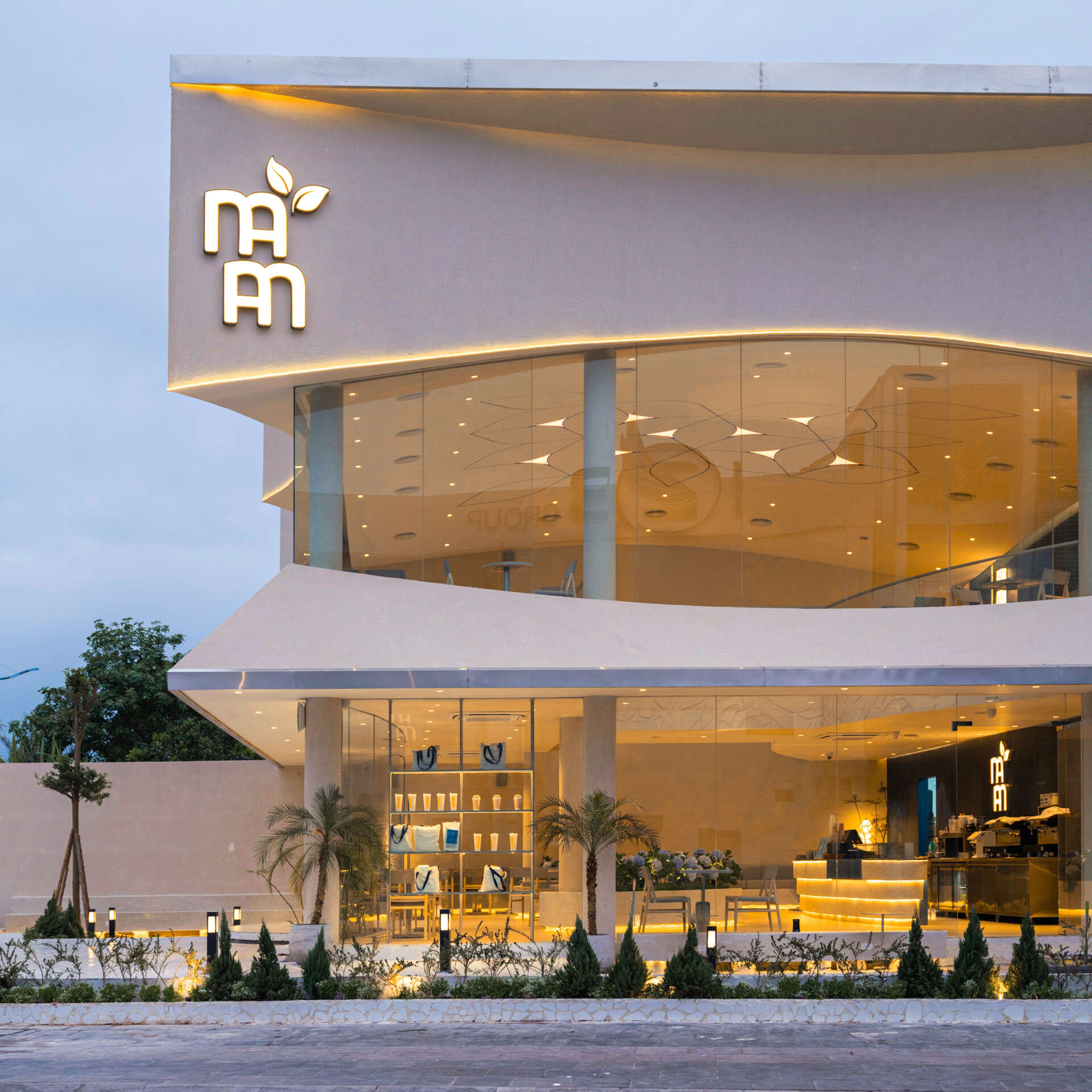 Inspired by the shape of a boat and featuring sweeping curved glass, soft flowing ceilings, and a calming neutral interior, this contemporary tea house celebrates one of Vietnam's most spectacular natural landscapes through architecture.