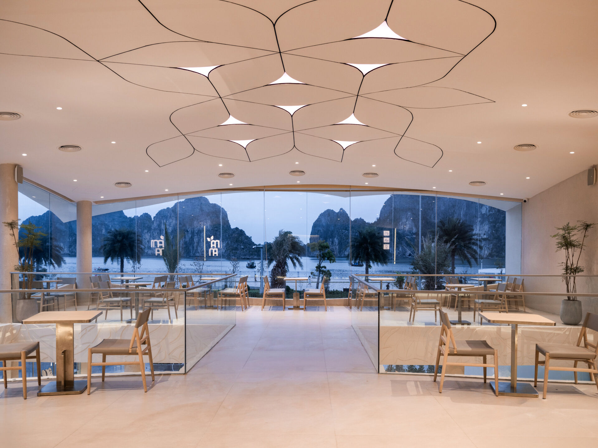 Inspired by the shape of a boat and featuring sweeping curved glass, soft flowing ceilings, and a calming neutral interior, this contemporary tea house celebrates one of Vietnam's most spectacular natural landscapes through architecture.