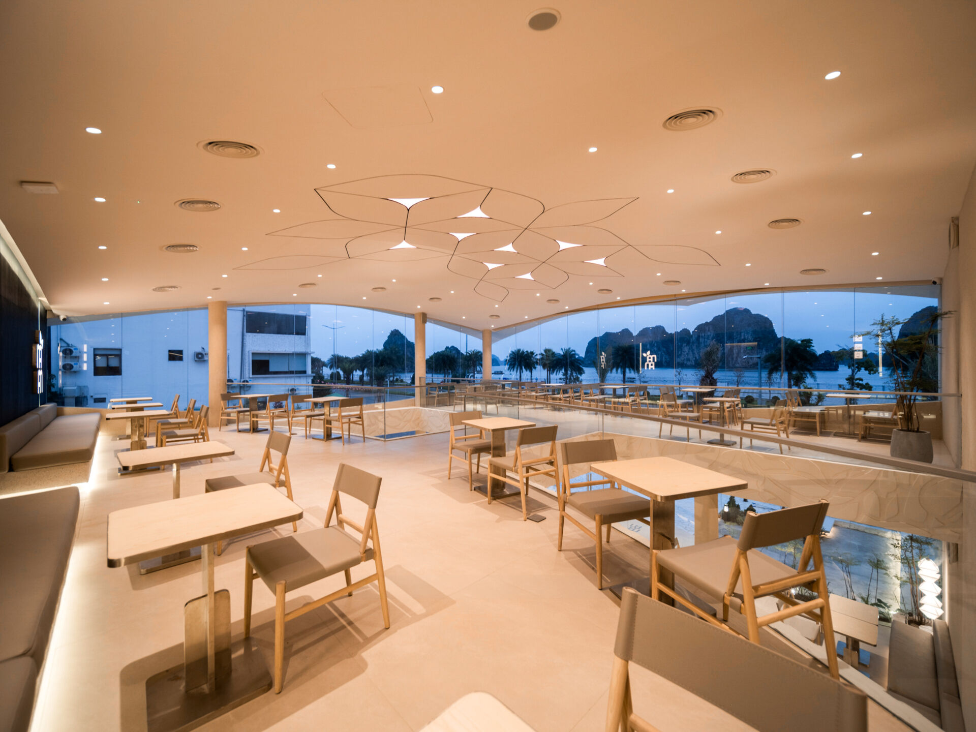 Inspired by the shape of a boat and featuring sweeping curved glass, soft flowing ceilings, and a calming neutral interior, this contemporary tea house celebrates one of Vietnam's most spectacular natural landscapes through architecture.