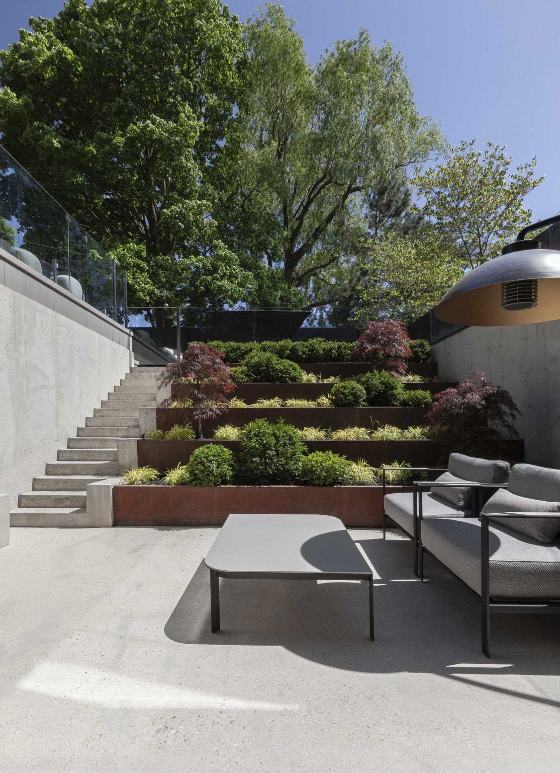 The backyard of Stack House features a swimming pool, outdoor dining area, patio, and terraced garden with weathered steel planters. A layered landscape design complements the bold architecture.