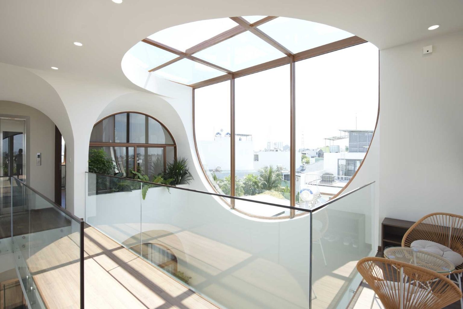 A rooftop garden, curved skylight window, and outdoor seating area crown this narrow Vietnam home with a bright and relaxing upper level.