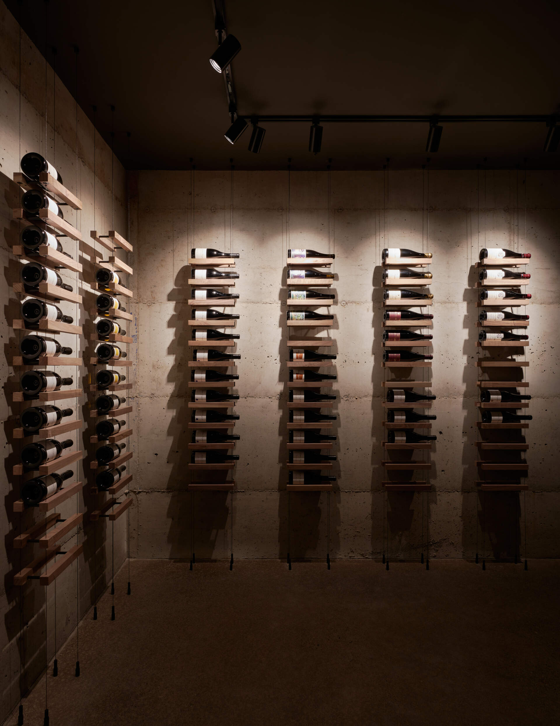 A modern wine cellar with concrete walls and suspended wood shelving for each wine bottle.