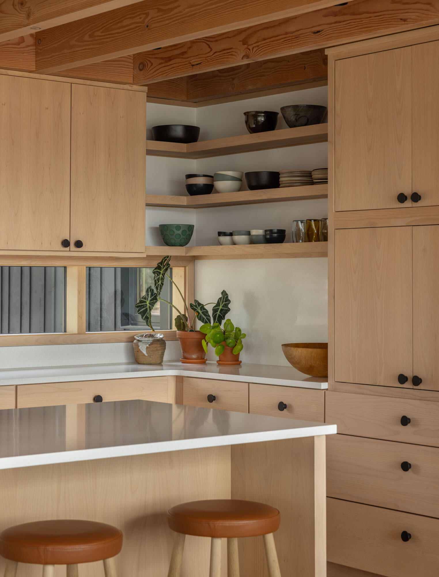 A warm and functional kitchen sits at the heart of this waterfront family home, surrounded by natural materials and inlet views.