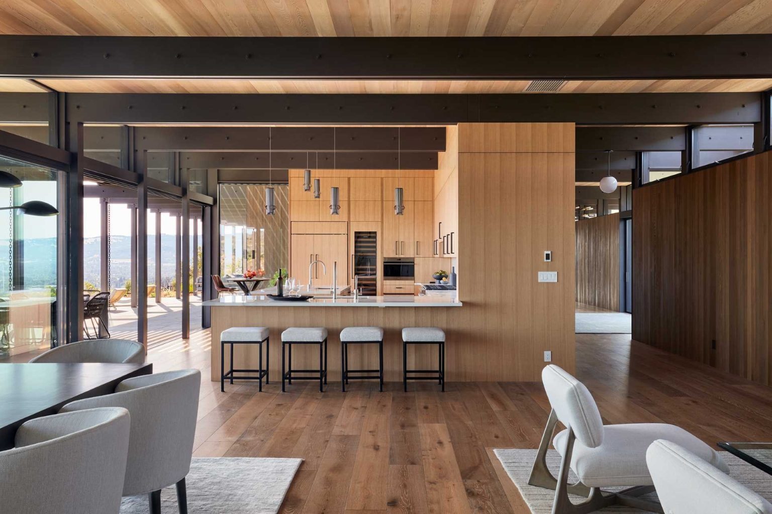 A continuous wood wall links the entry and kitchen, where tall cabinetry, pendant lighting, and light counters create a welcoming space.